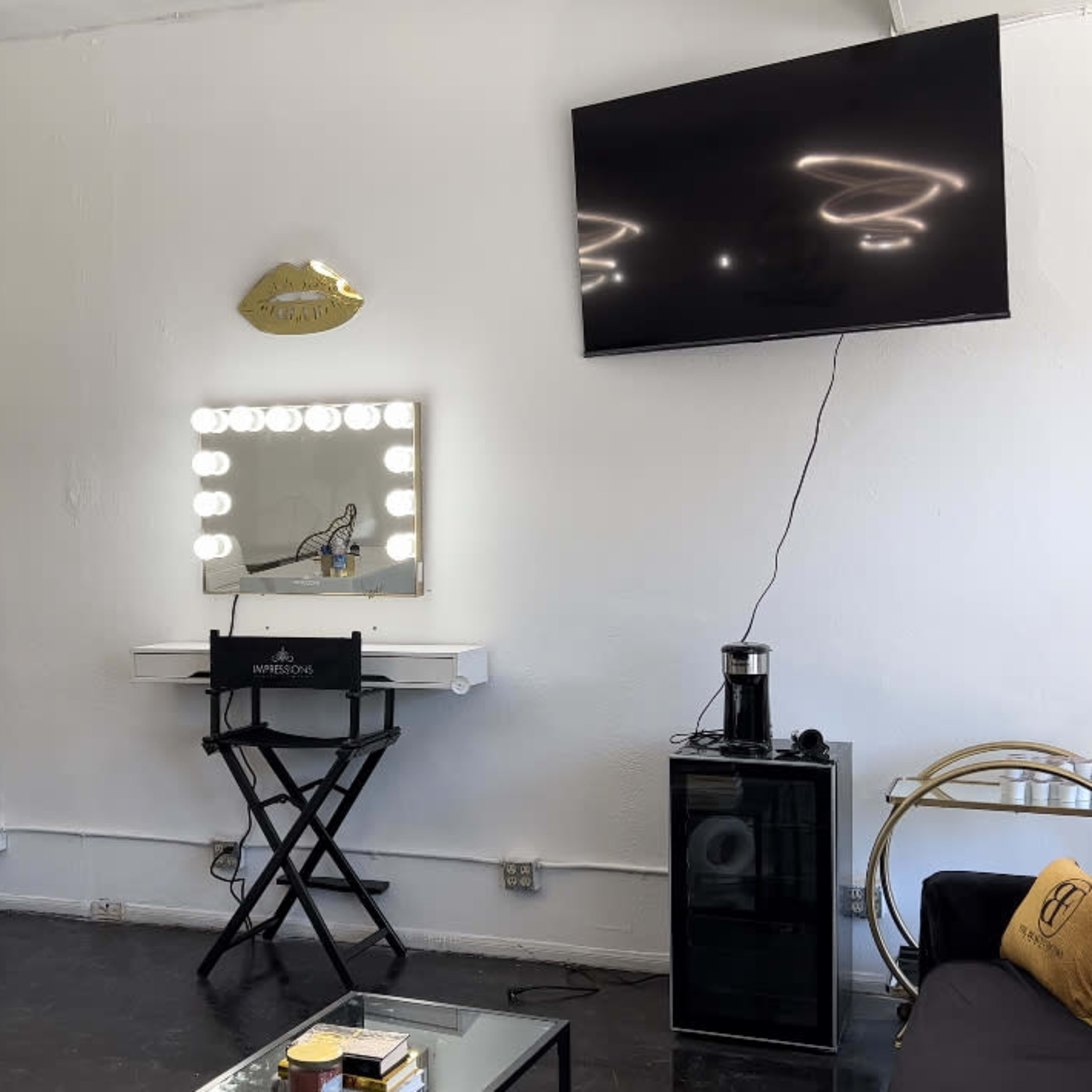 A modern salon interior featuring three mirrors, a large television mounted on the wall, and a seating area with a coffee table.