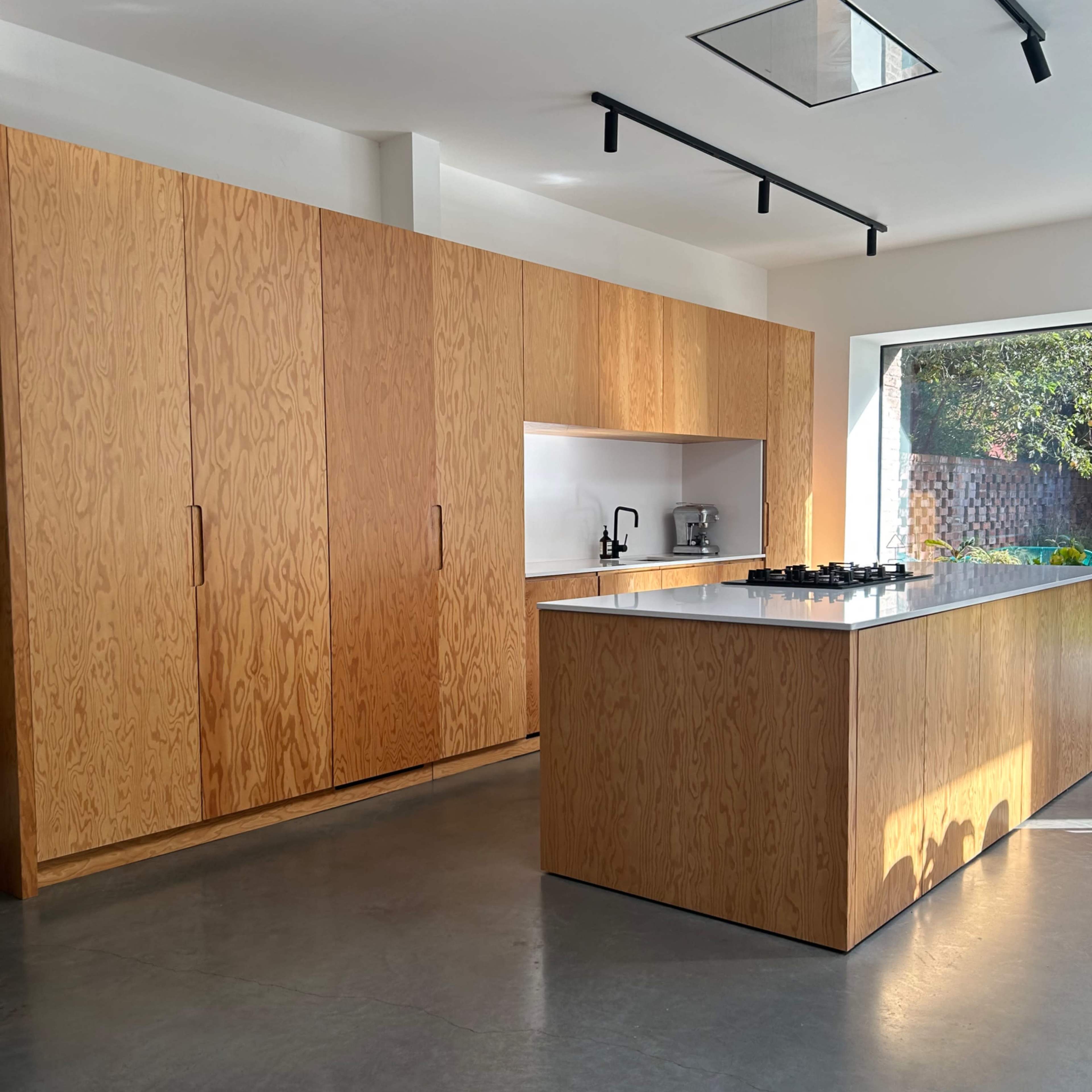 The kitchen features light wood cabinetry, a central island with a gas cooktop, and a large window providing natural light.
