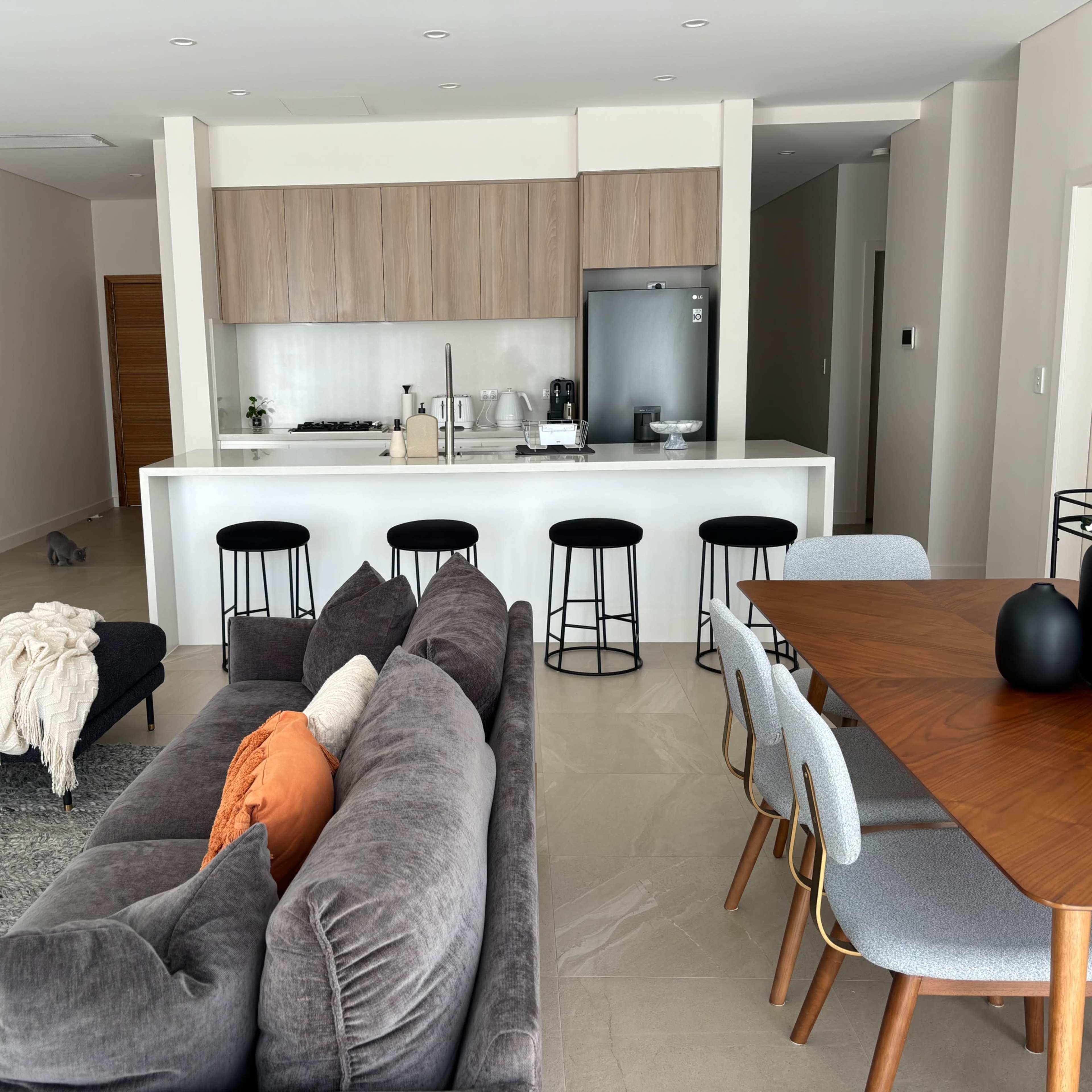 A modern open-concept living area with a sofa, dining table, and a kitchen in a bright, minimalist design.