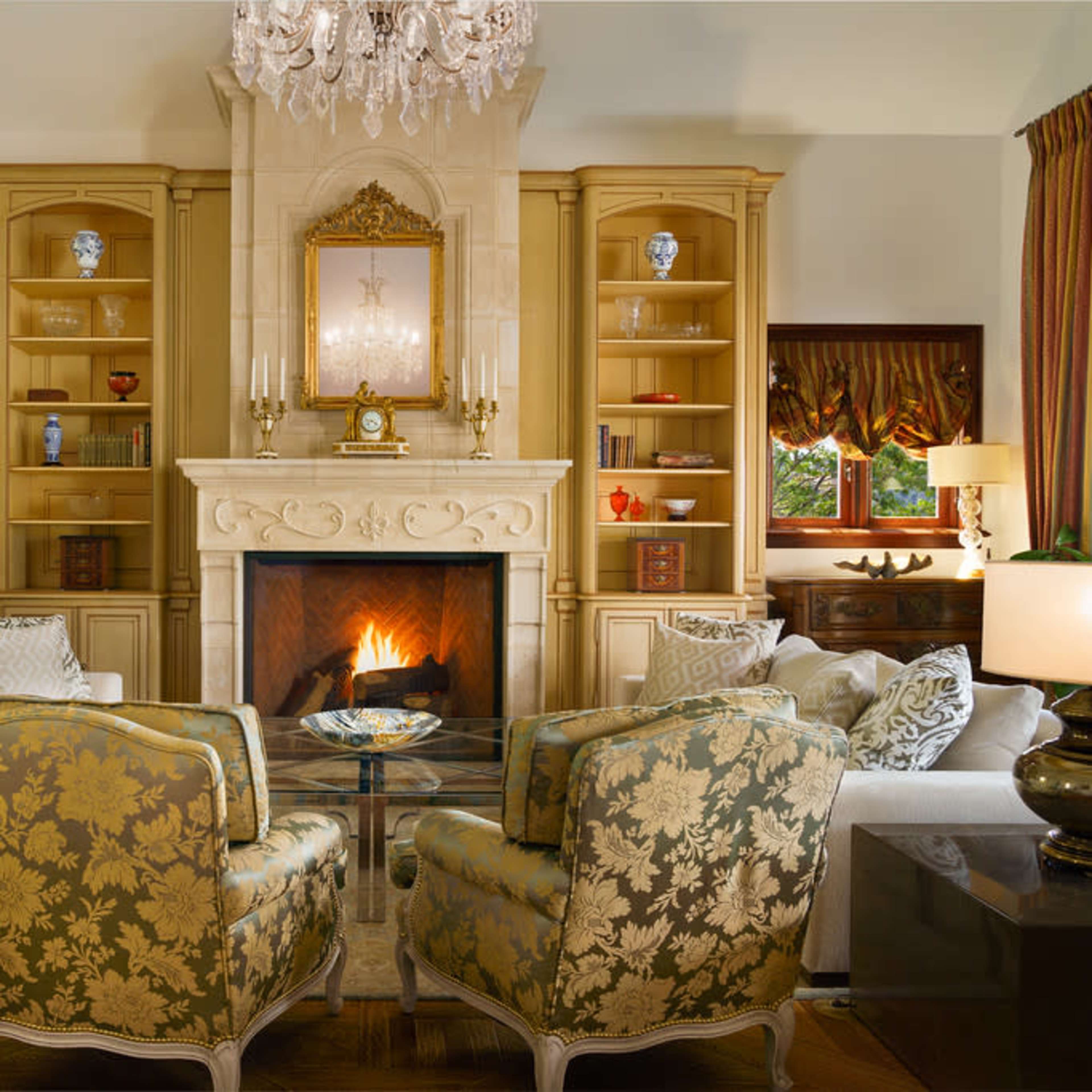A elegantly furnished living room with a central fireplace, two patterned armchairs, and built-in shelves displaying decorative items.