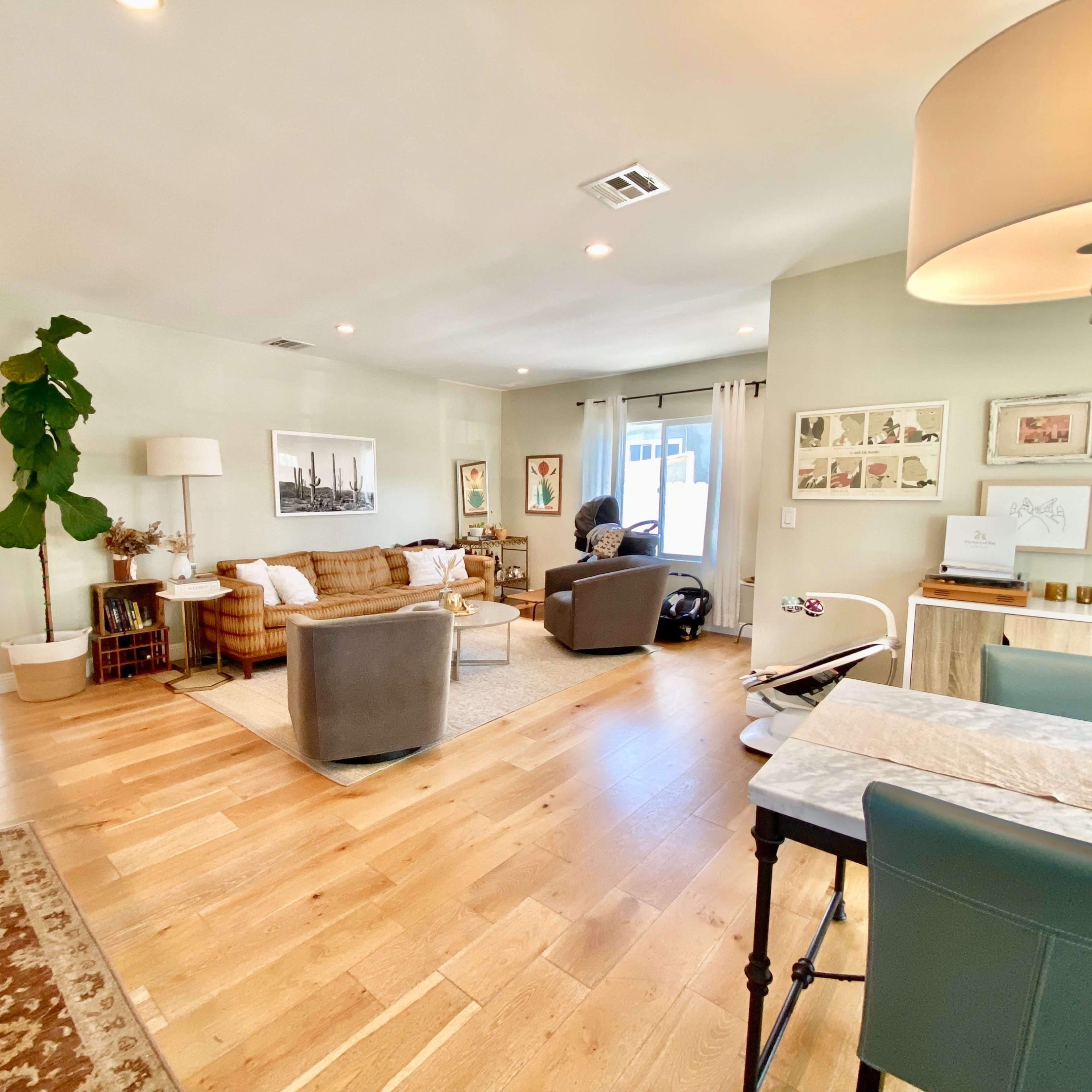 A spacious living room area featuring a couch, armchairs, artwork on the walls, a dining table, and a plant in the corner.