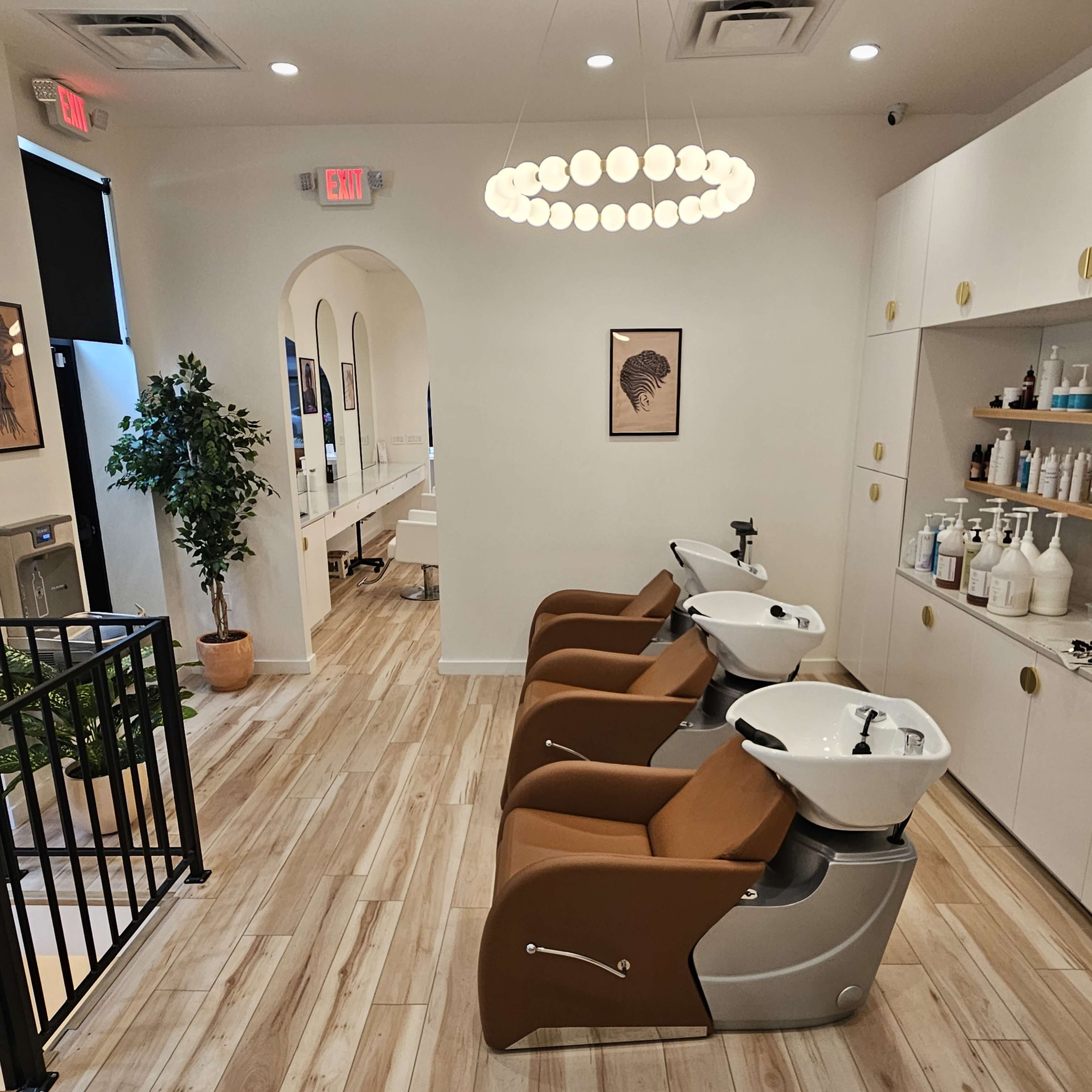 A modern salon interior with three shampoo stations, light wood flooring, and a round pendant light.