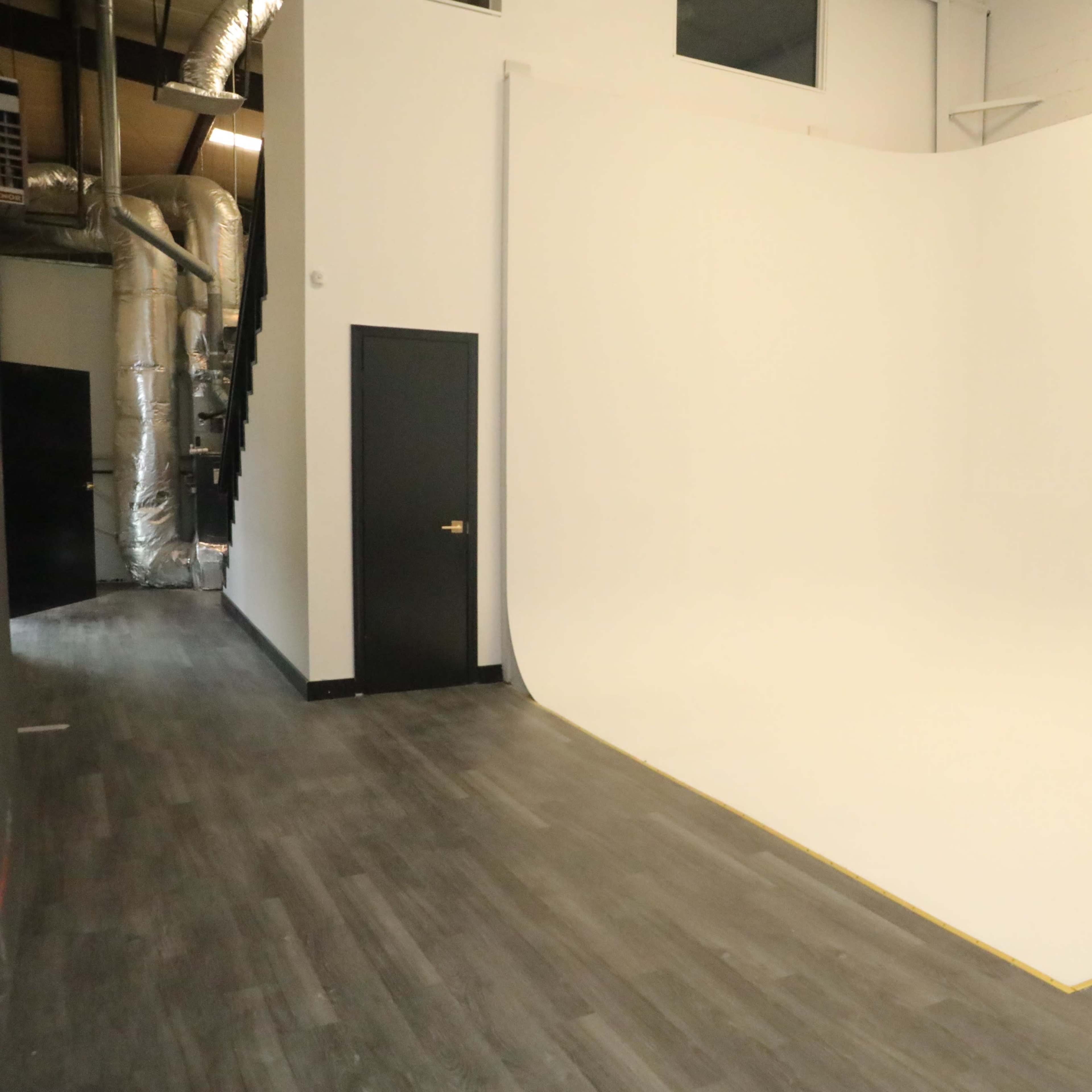 A spacious photo studio with a curved white backdrop and wooden flooring.