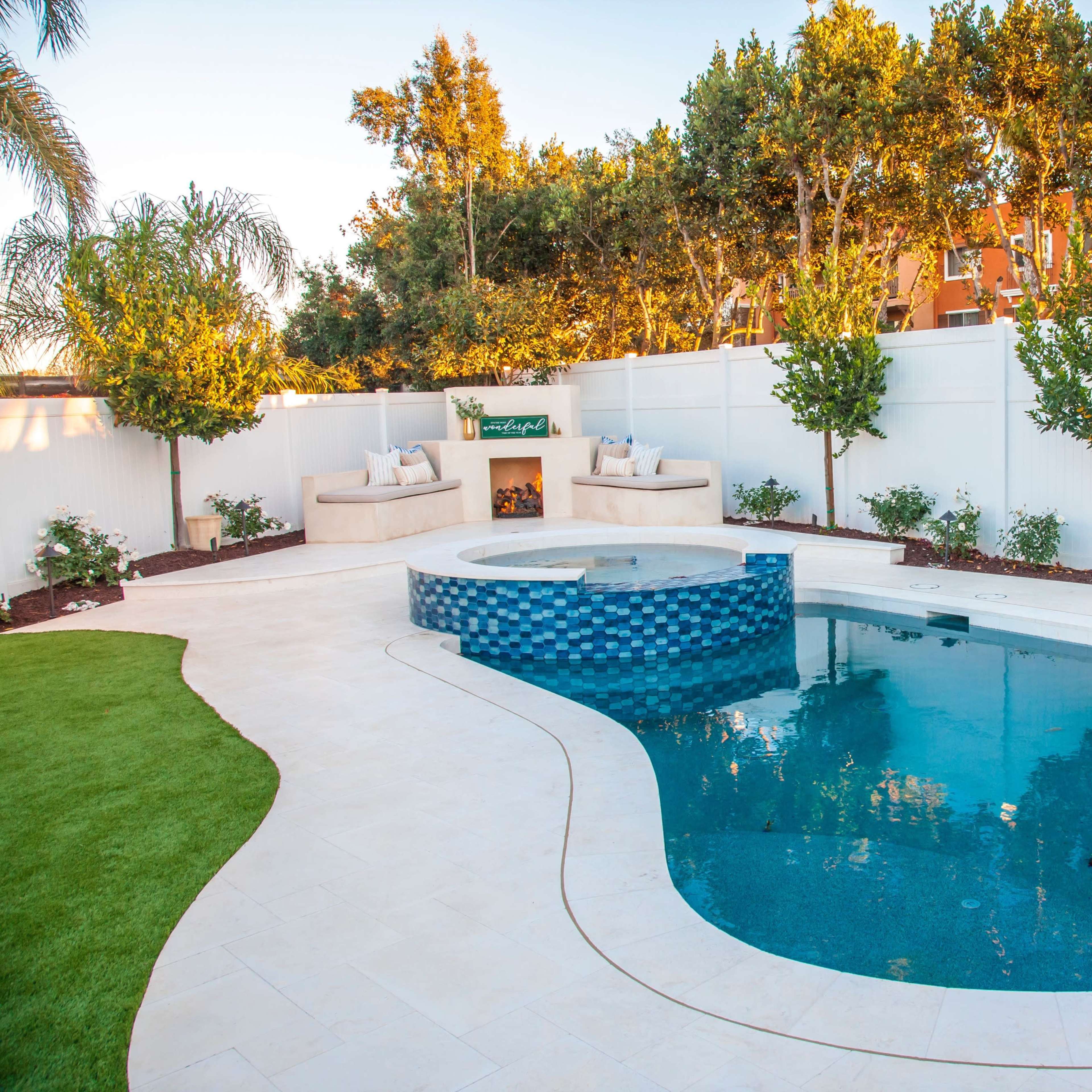A backyard features a curved swimming pool with blue tiles, a spa area, and landscaped surroundings with lush greenery and seating.