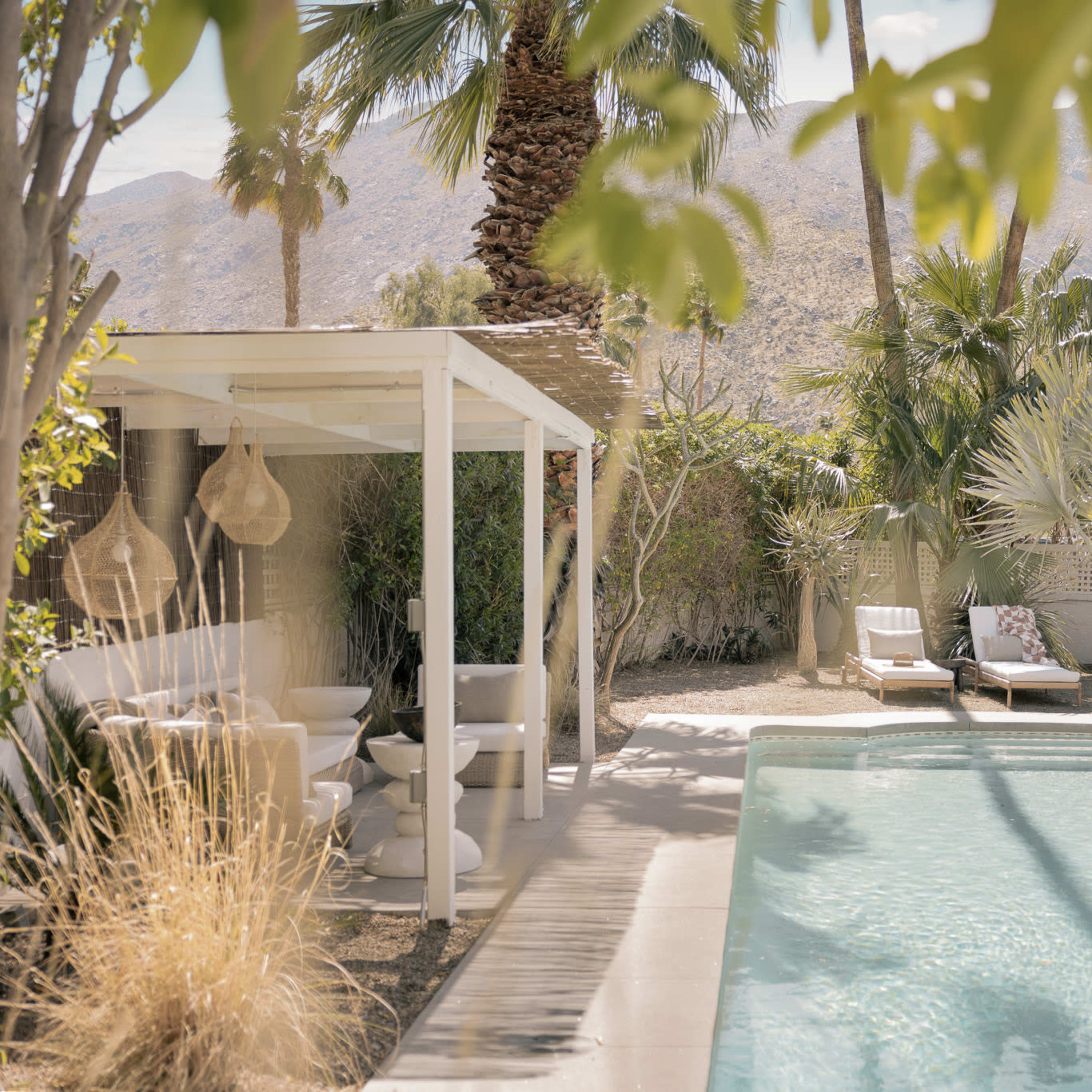 A serene outdoor pool area surrounded by palm trees and lush greenery, with lounge chairs and a shaded structure nearby.