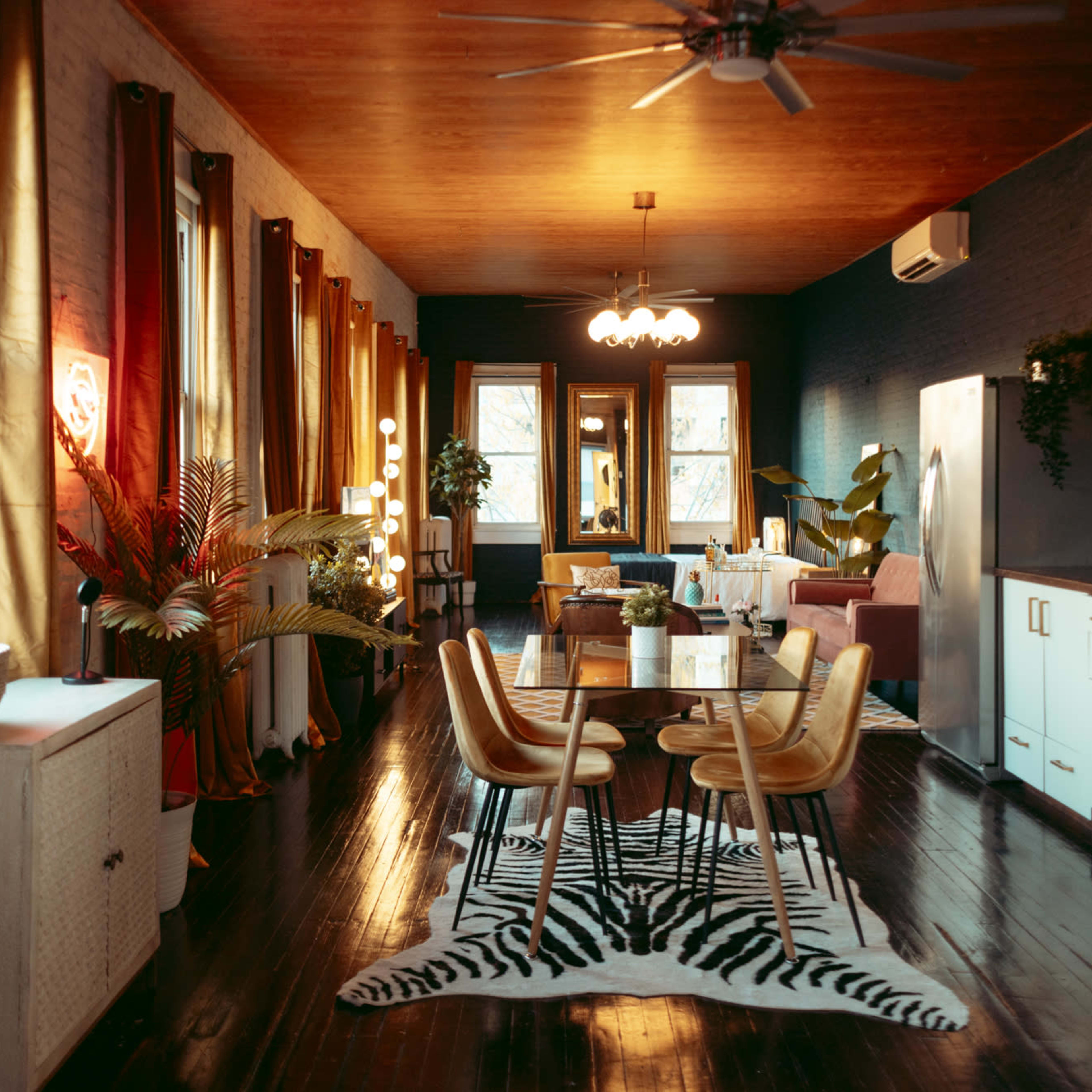 A modern living space with wooden floors, large windows, a dining table, and a blend of contemporary furniture and plants.