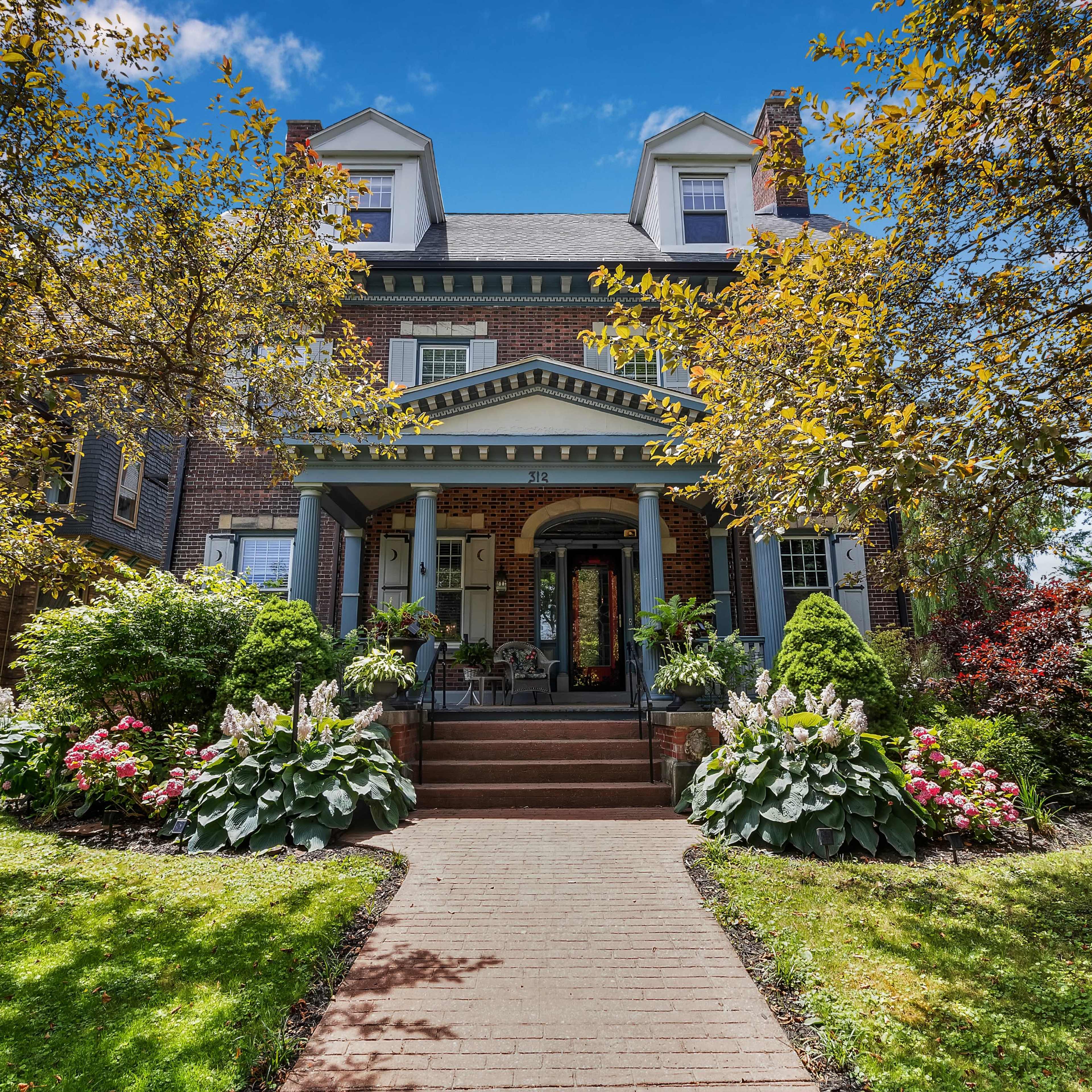 A large brick house with a front porch, surrounded by well-maintained gardens and trees.