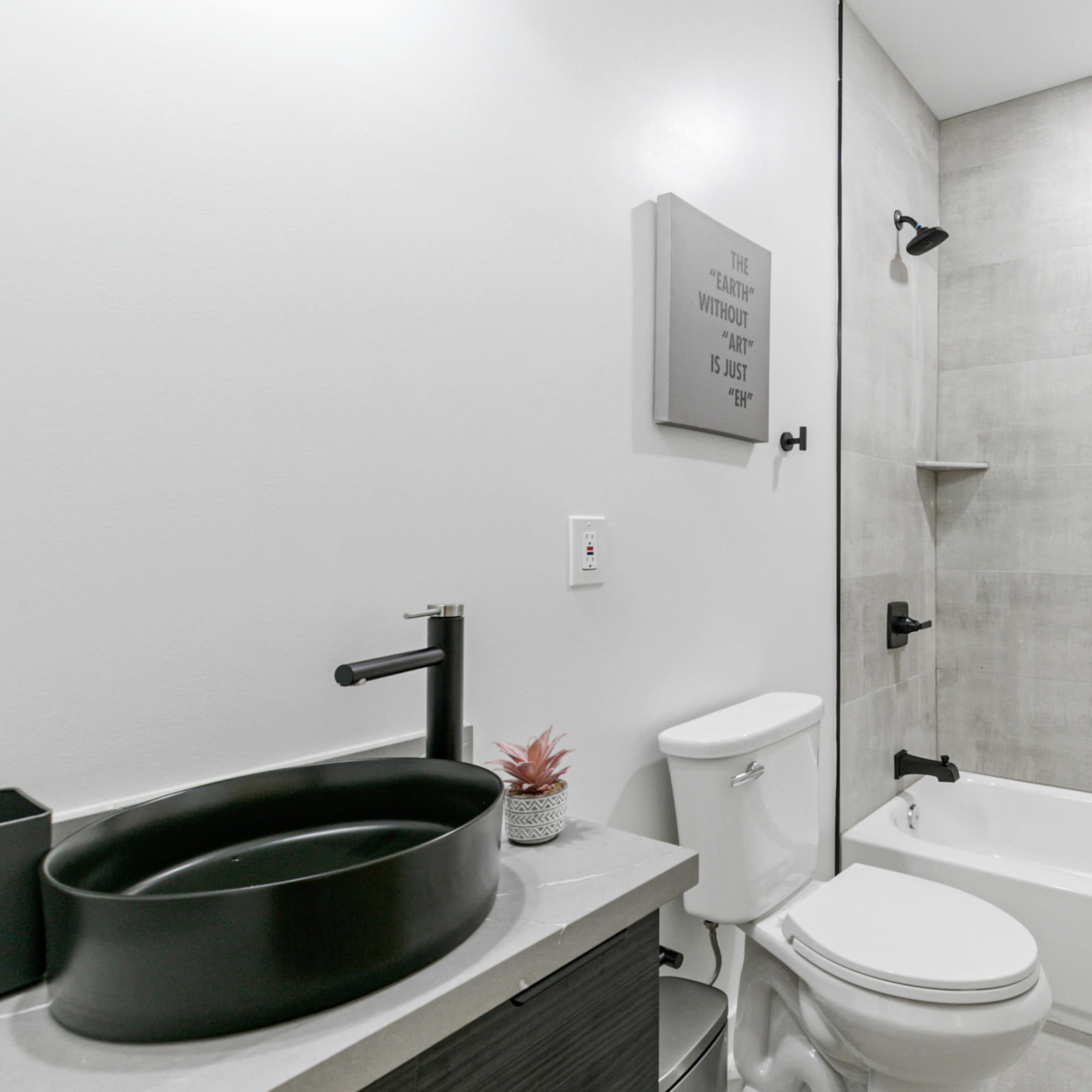 A modern bathroom featuring a shower tub combination, a black circular sink on a dark countertop, and minimalistic decor.
