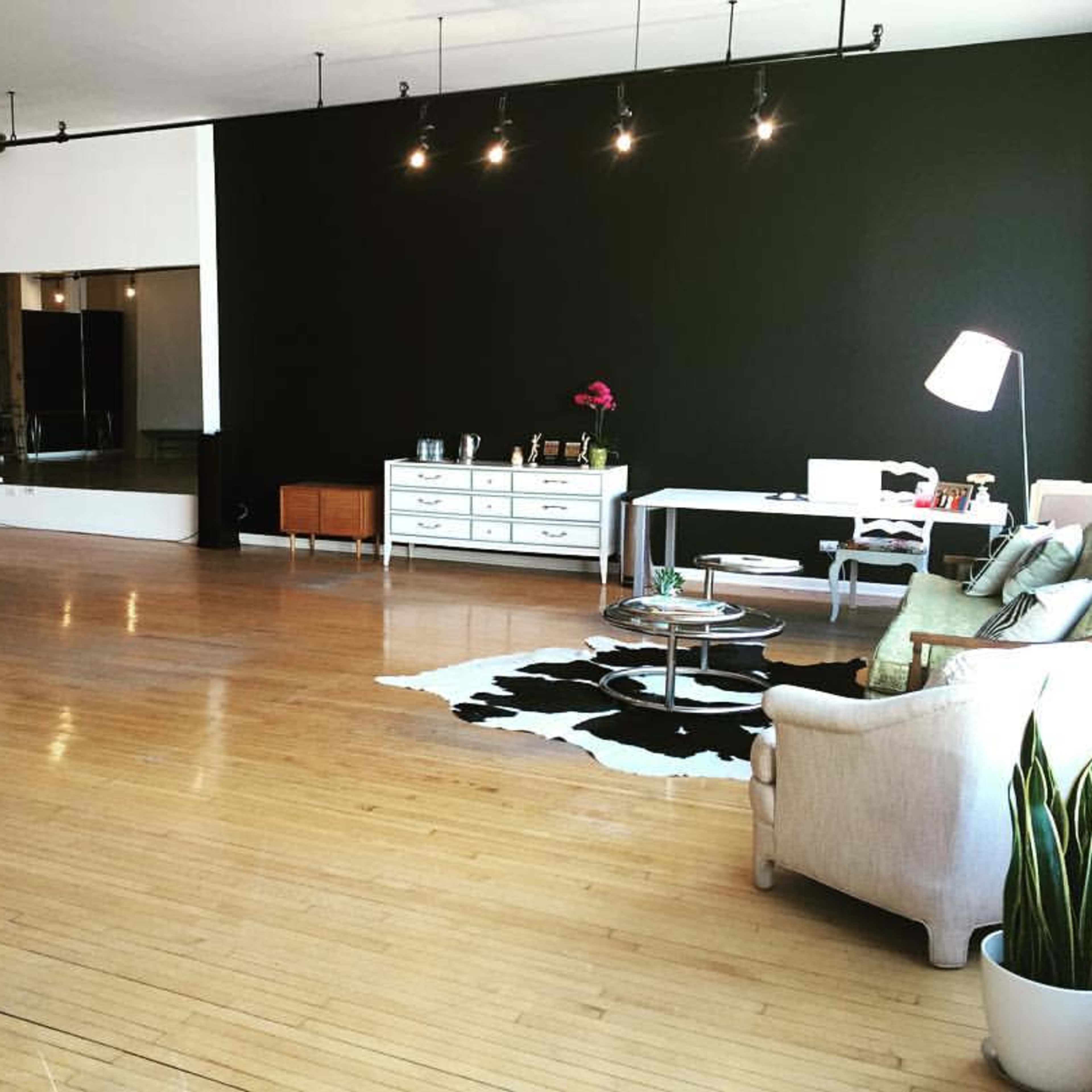 A spacious studio with dark green walls, wooden flooring, a seating area, a large mirror, and a desk against one wall.