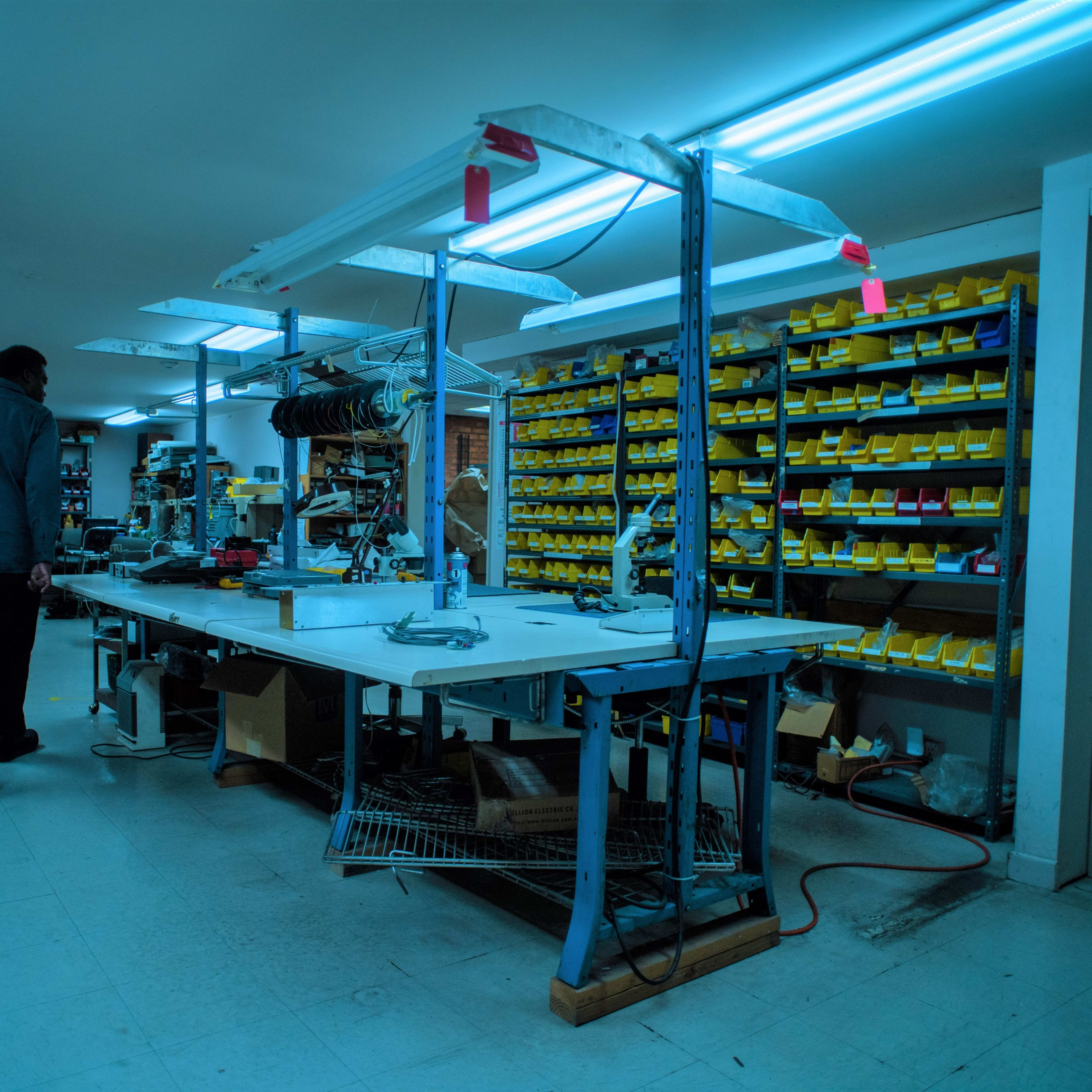 A person walks through a dimly lit workshop filled with tools, equipment, and neatly organized yellow storage bins along the walls.