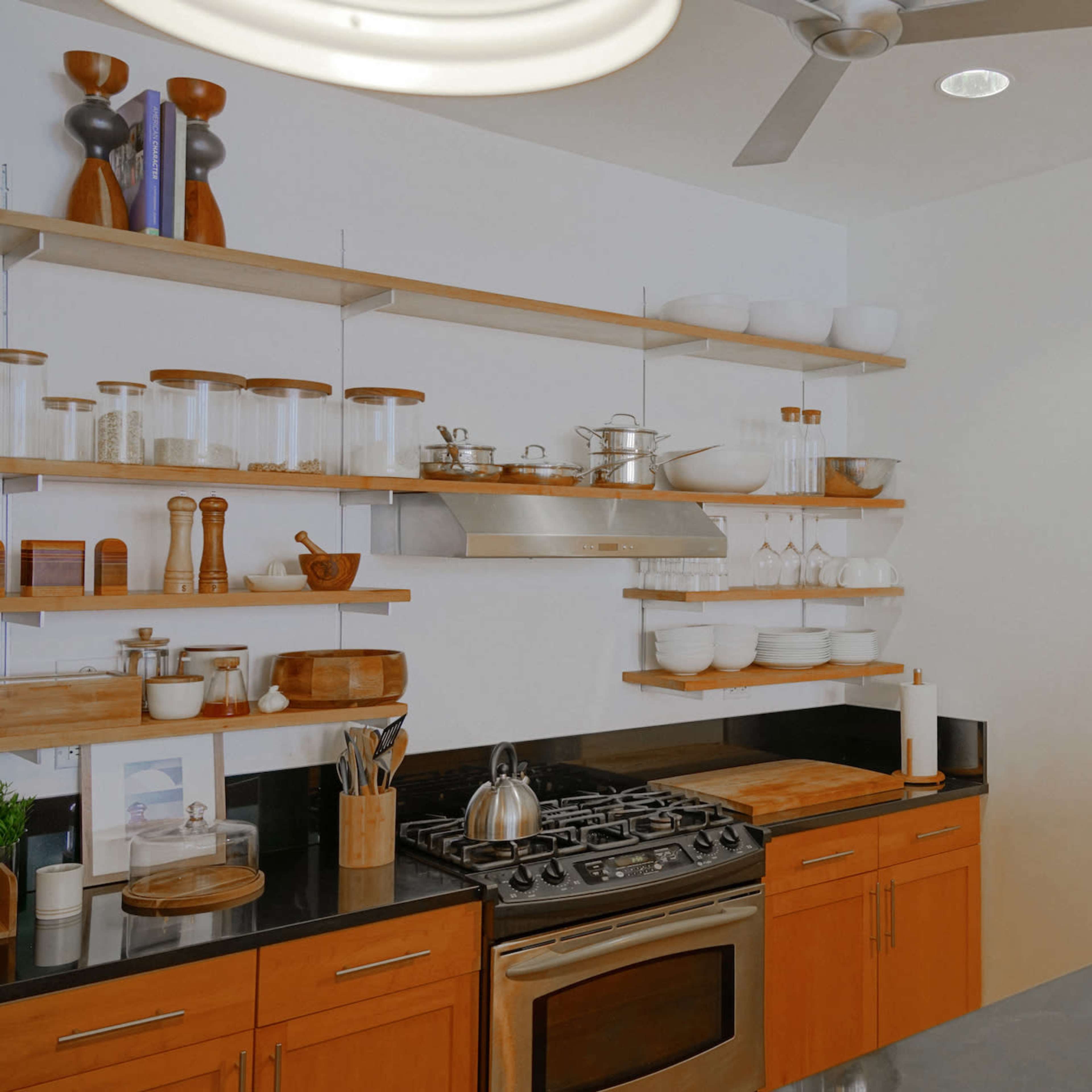 A modern kitchen with open shelves displaying glassware and kitchen tools, a stainless steel stove, and a sleek countertop.