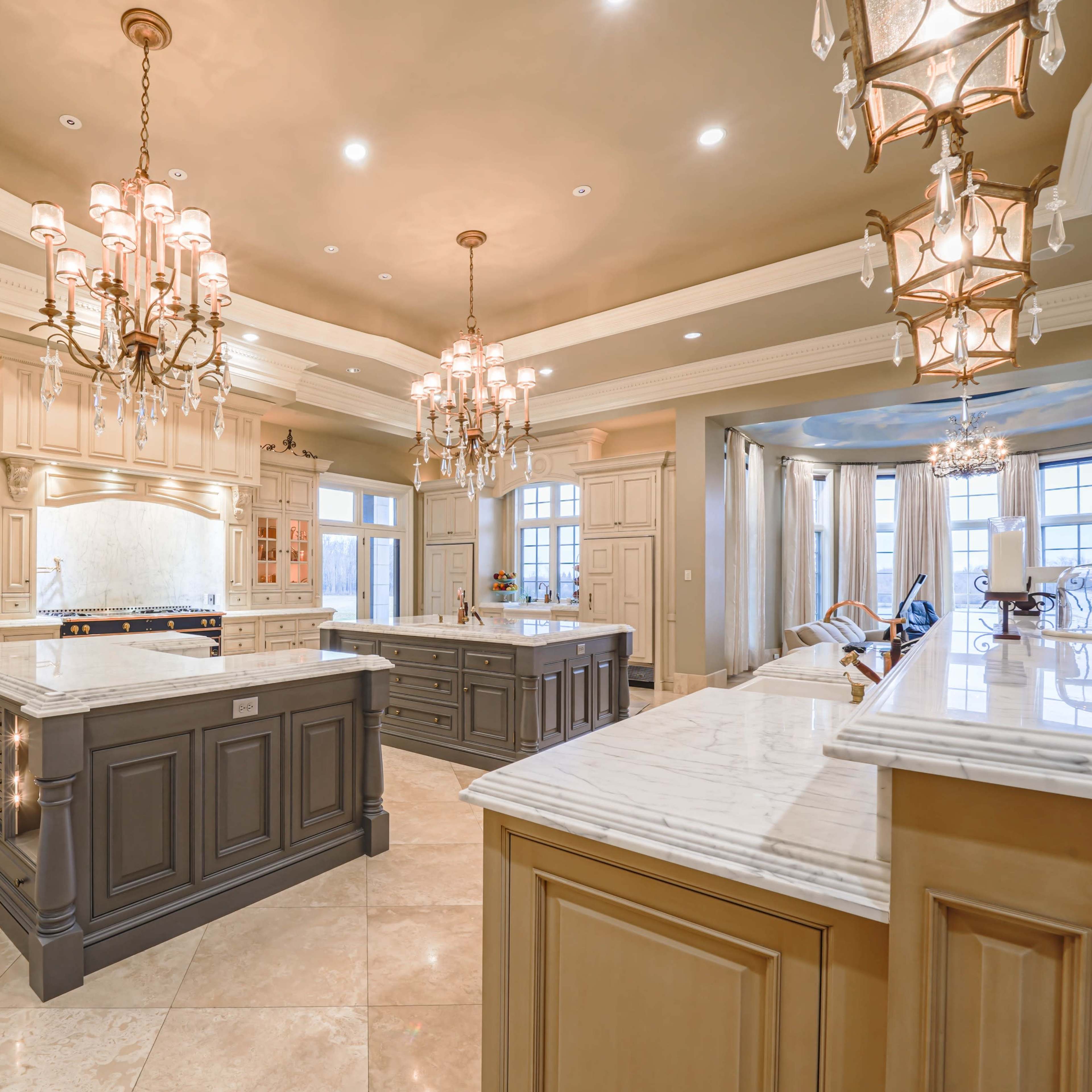 A spacious kitchen with multiple island countertops, elegant cabinetry, and several ornate light fixtures.