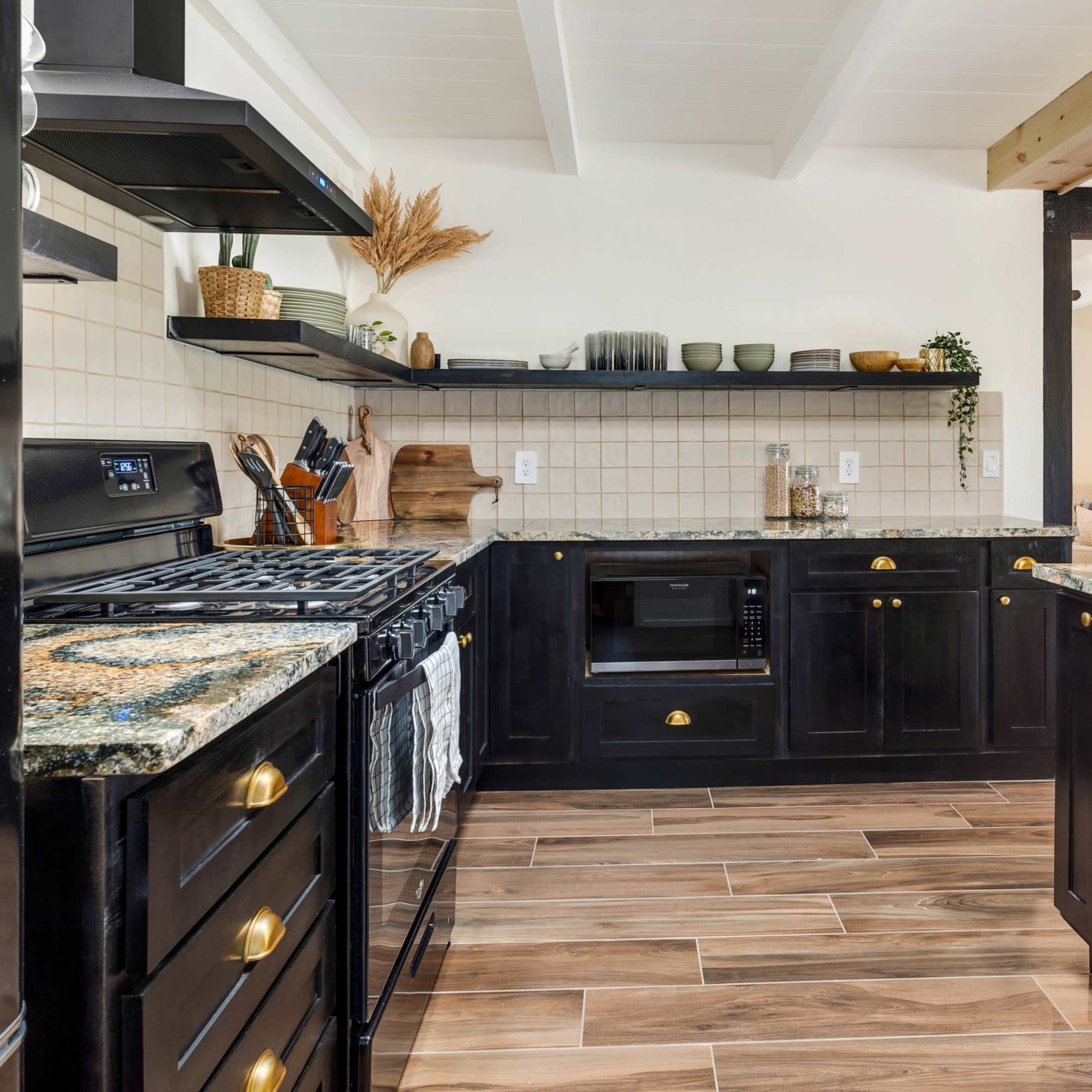 A modern kitchen featuring dark cabinetry, granite countertops, a gas stove, and open shelving with decorative items.