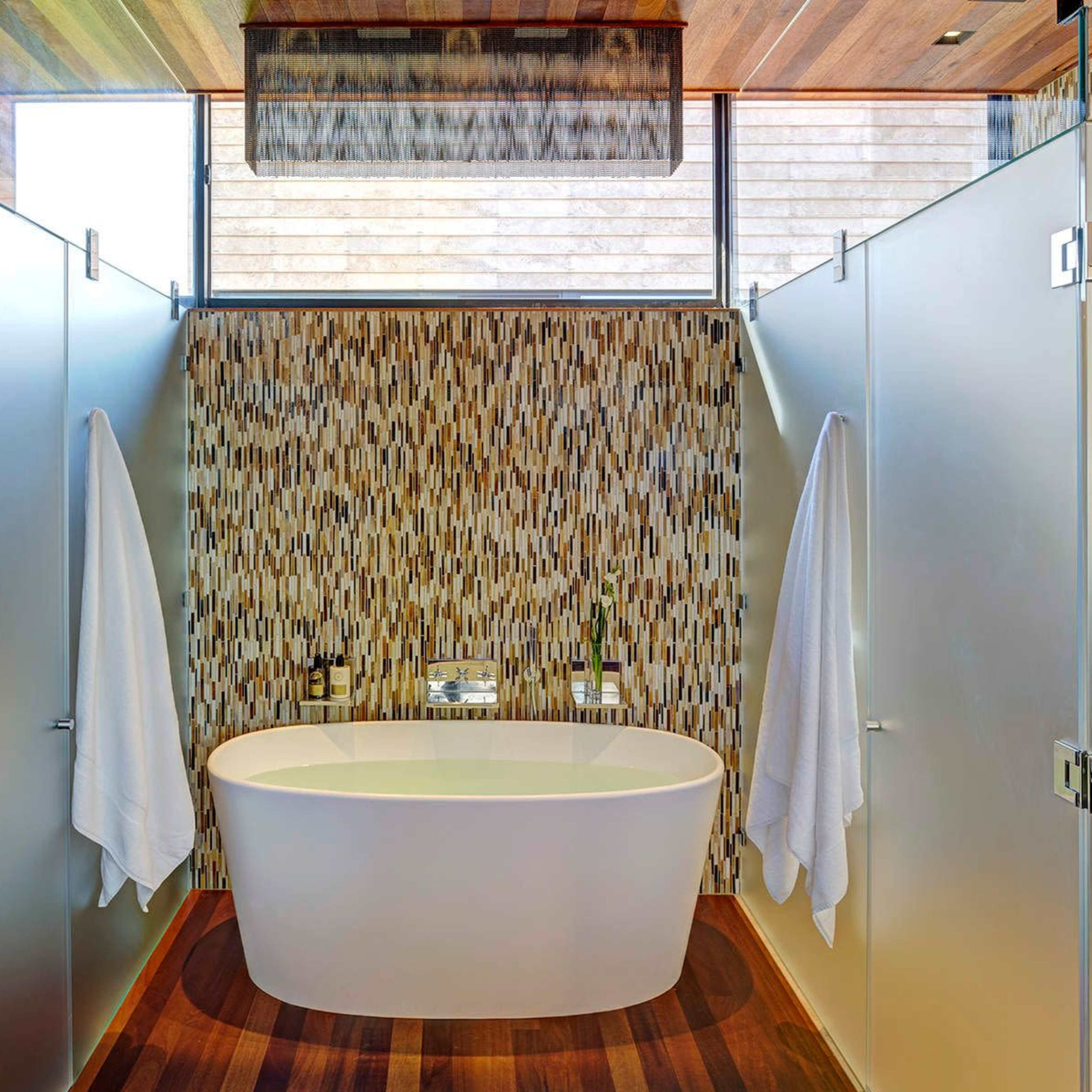 A modern bathroom with a freestanding bathtub surrounded by frosted glass partitions and a decorative wall.