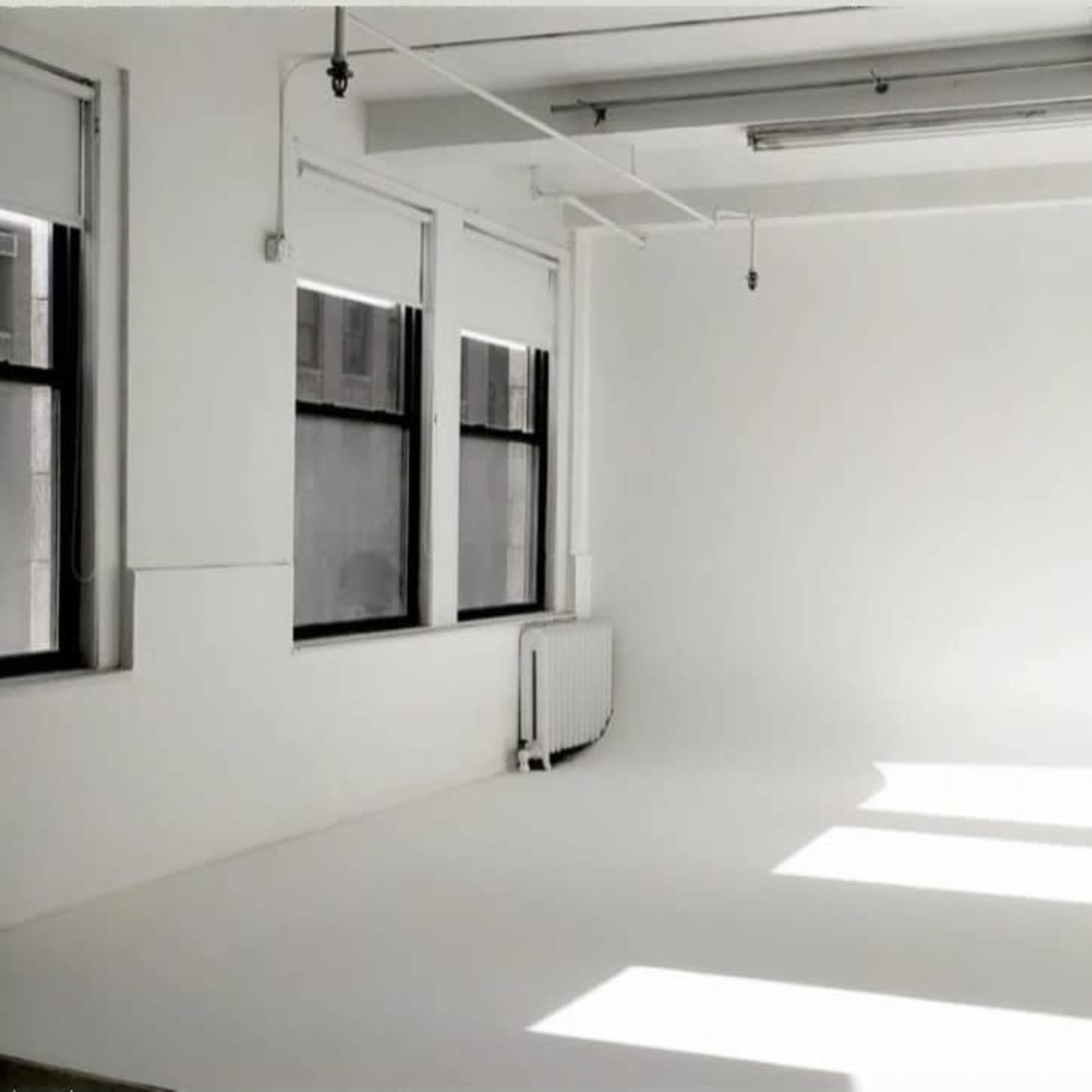 A spacious, bright room with white walls and large windows casting shadows on the floor.