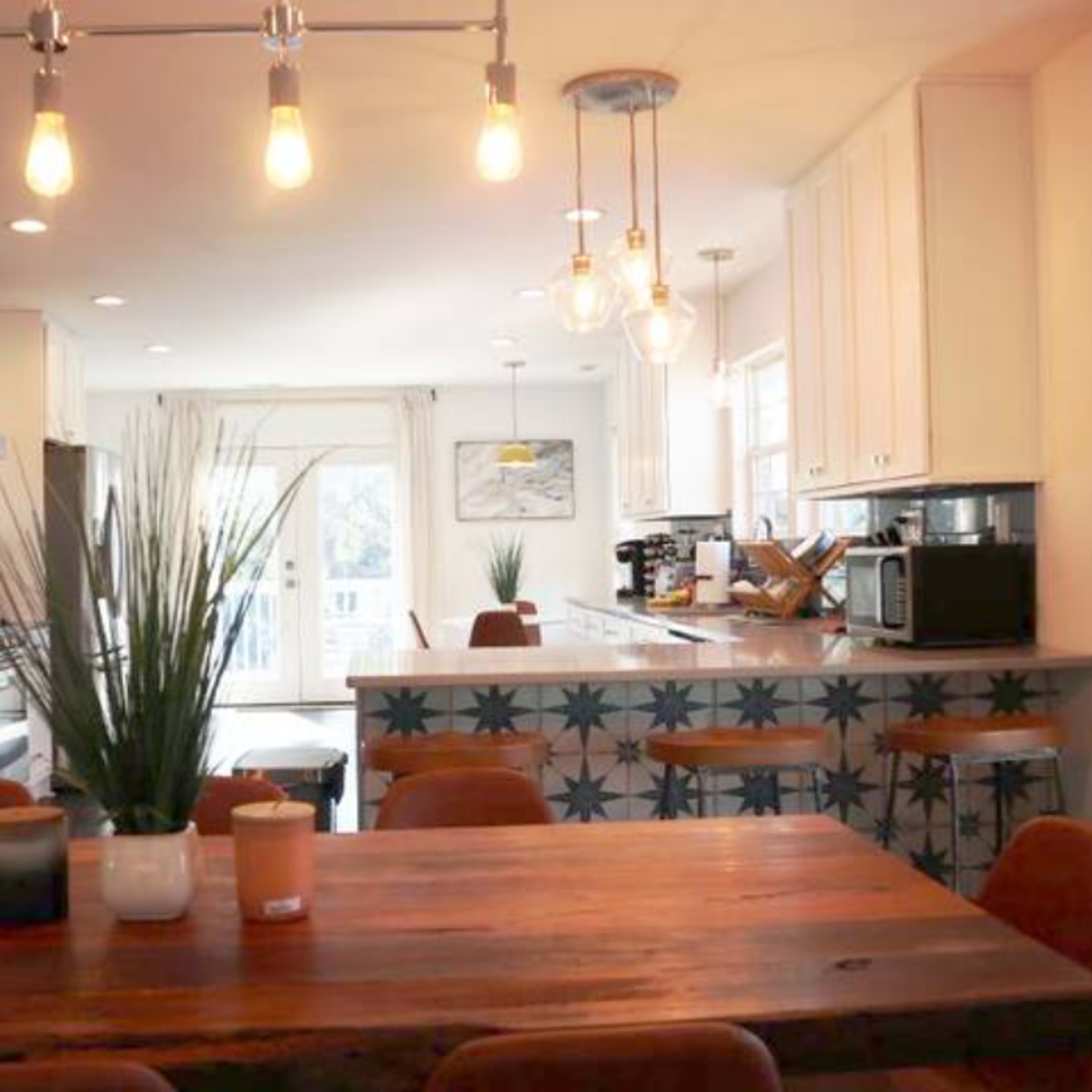 A modern kitchen with a dining table, featuring wooden surfaces and a well-lit atmosphere, complemented by minimalistic decor and bar stools at the counter.