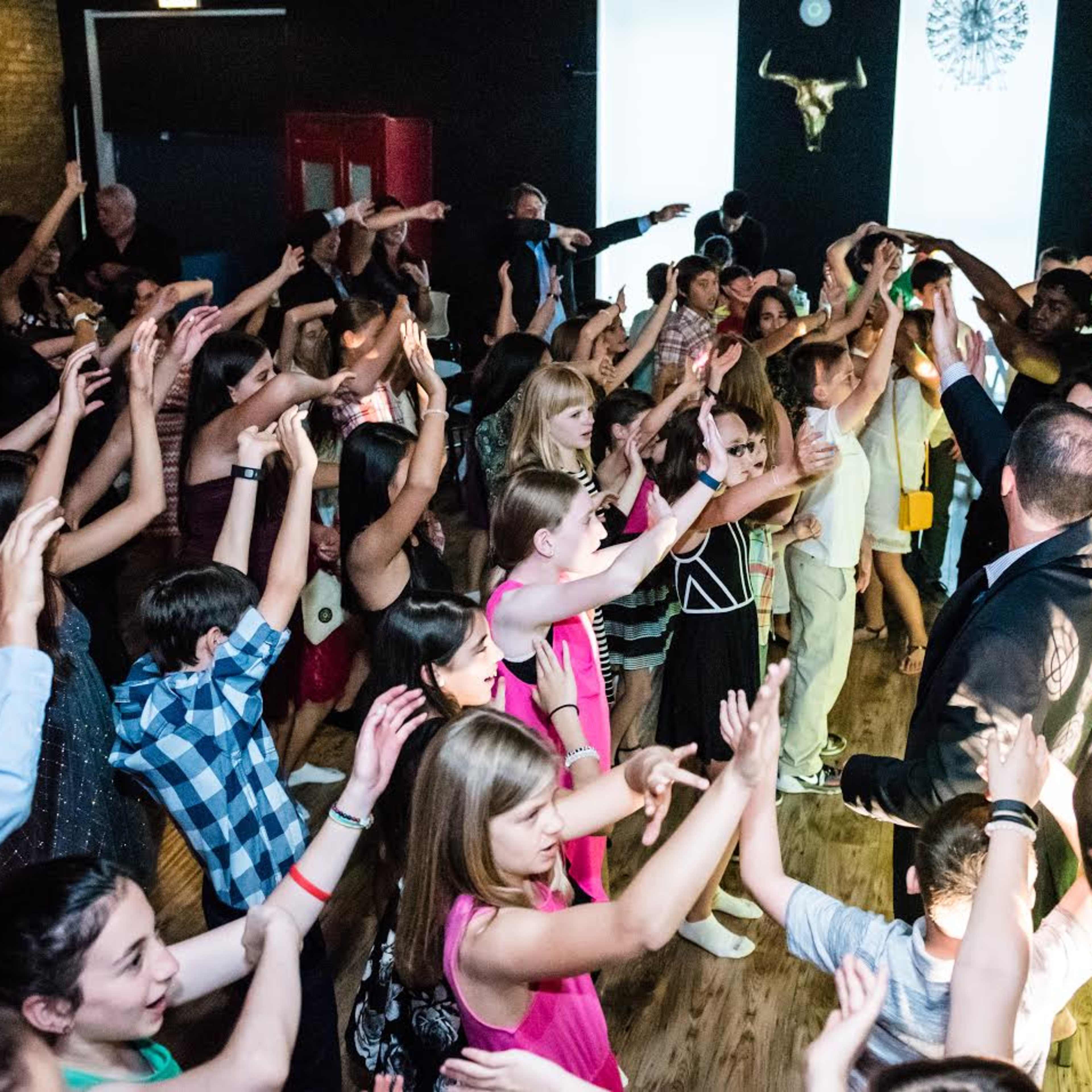 A large group of people dances with raised arms in a lively indoor venue.