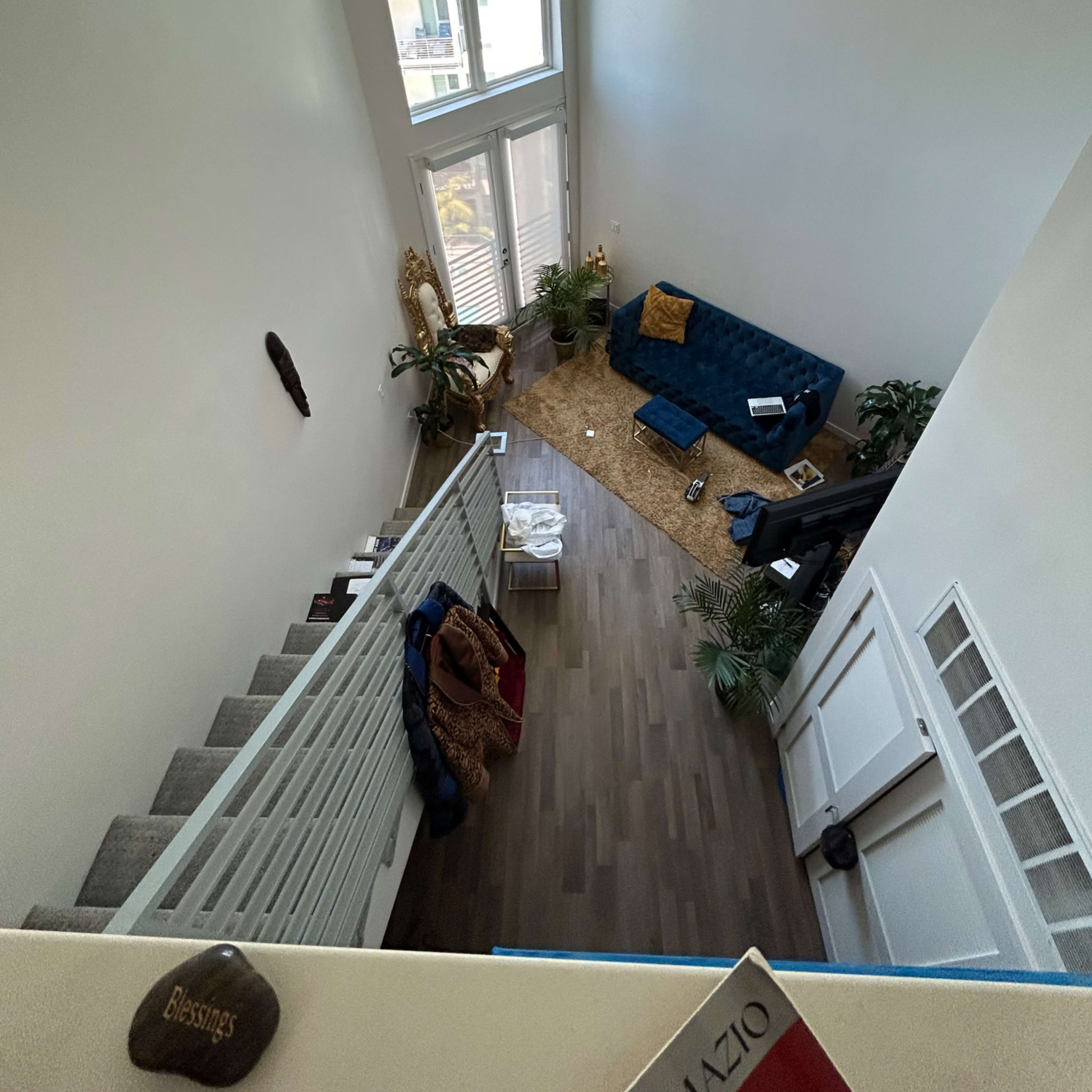 A spacious living area with a blue sofa, a large window letting in light, and a staircase leading down.