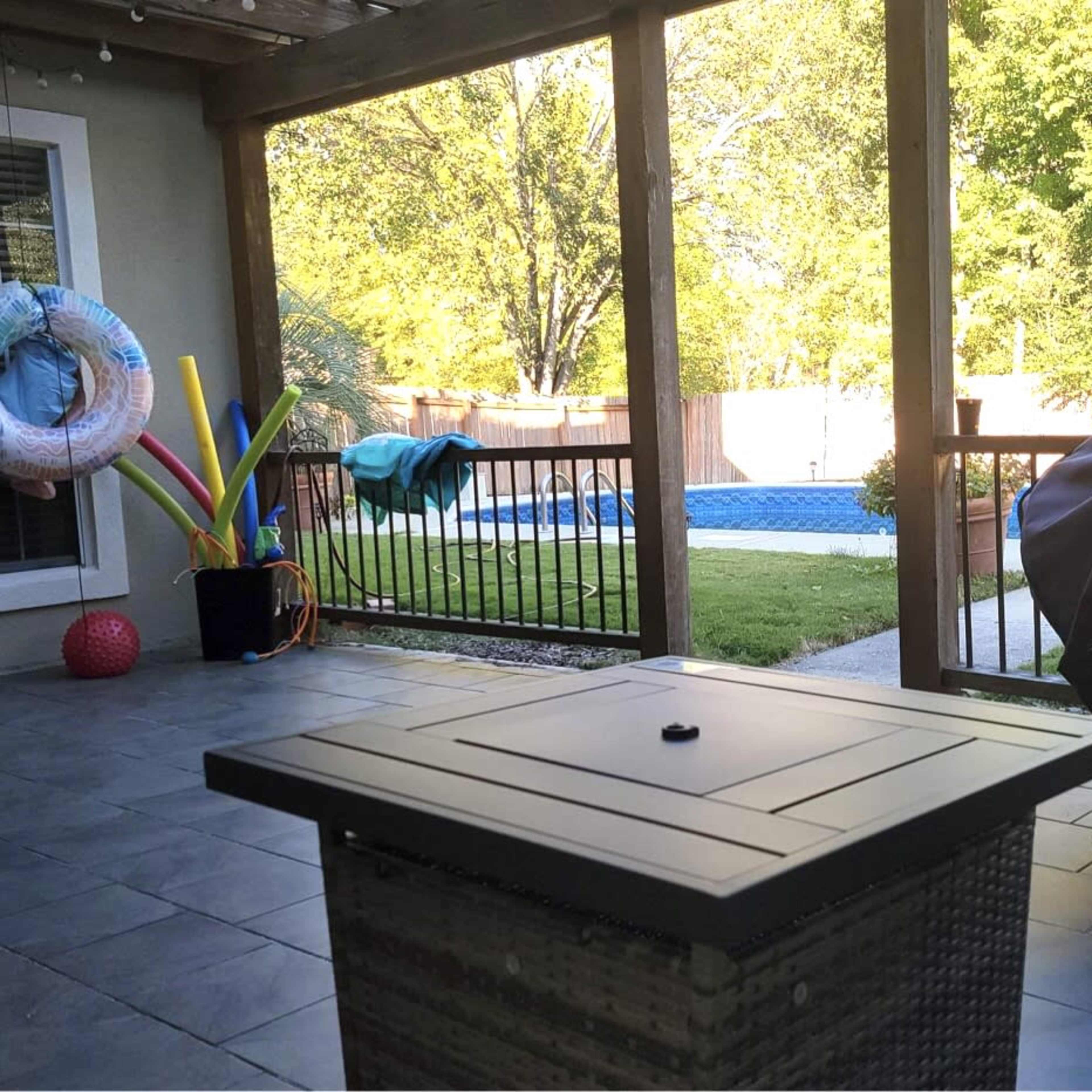 A patio area with a table at the forefront, viewing a backyard with a swimming pool and colorful pool toys nearby.
