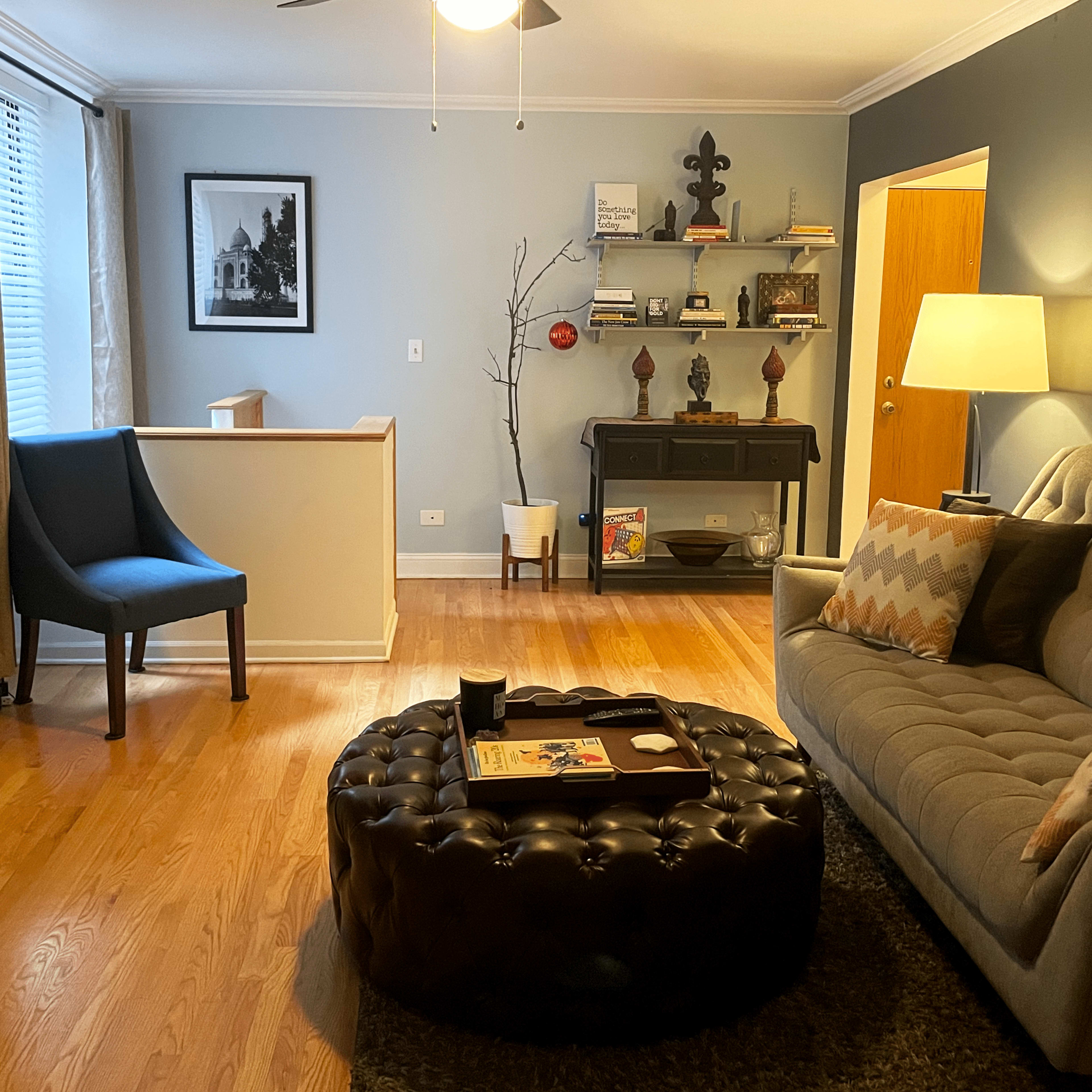 A living room with a gray couch, a round ottoman, a blue accent chair, and a wall-mounted television.