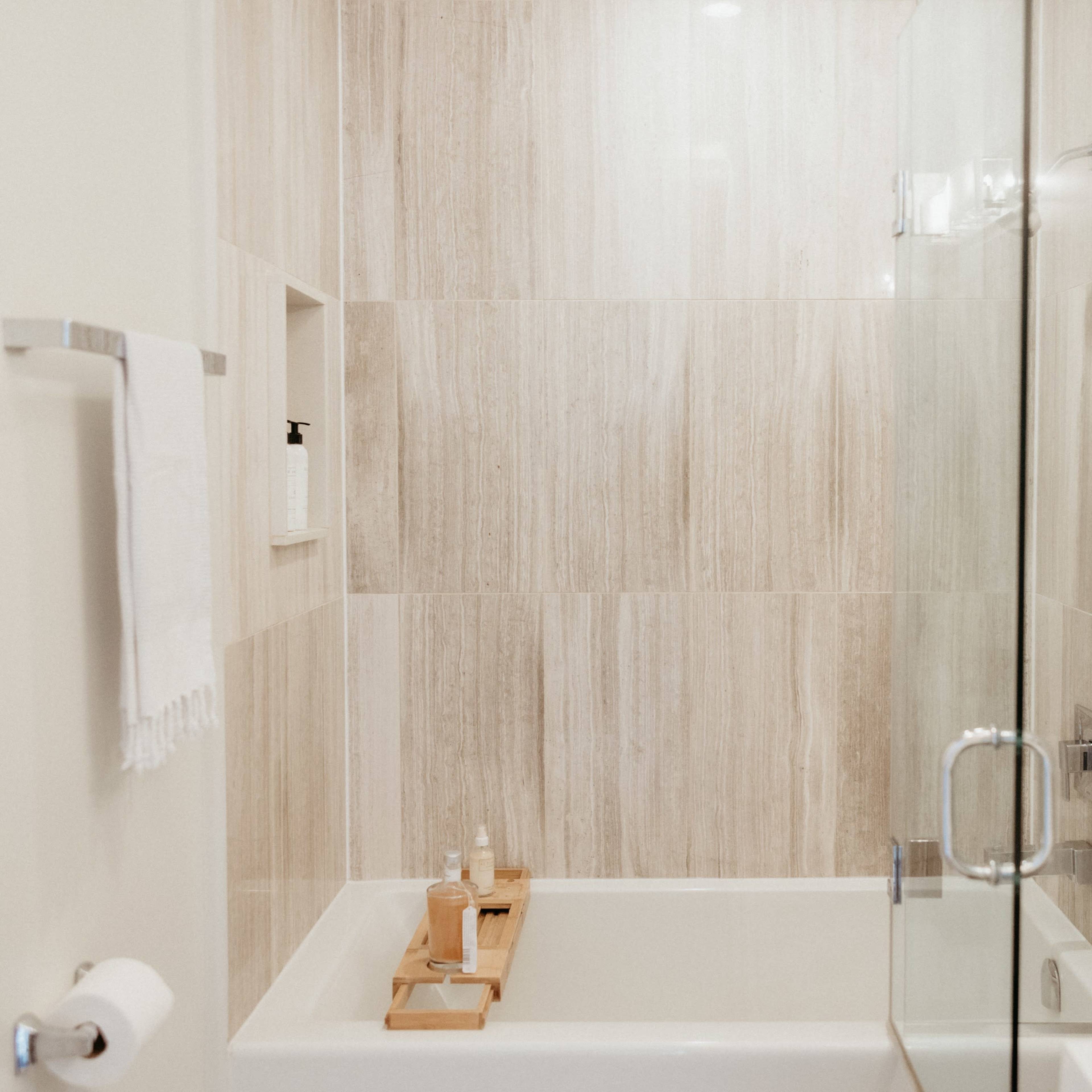A modern bathroom featuring a glass shower enclosure, a bathtub, and a wooden tray with toiletries on it.