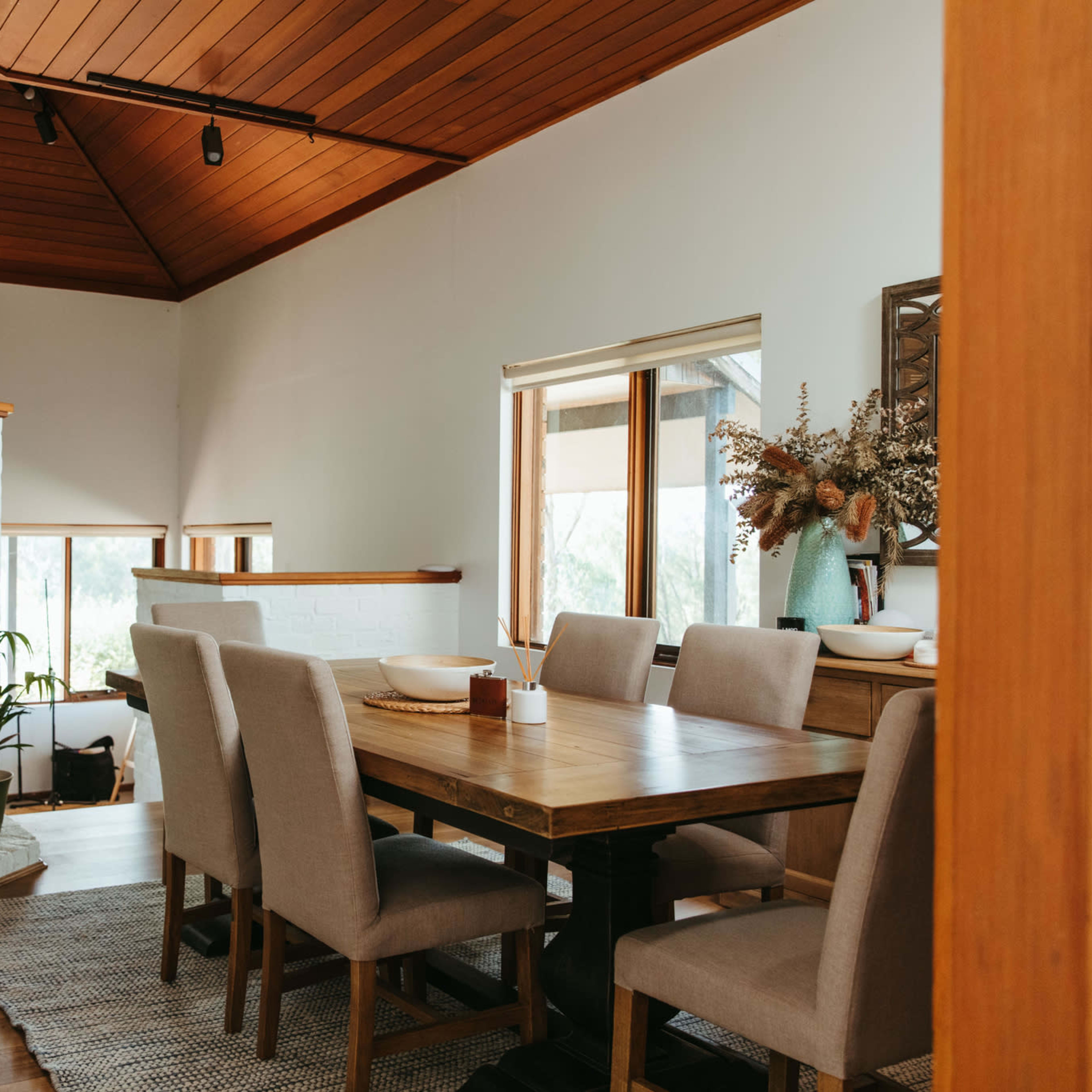 A dining area featuring a large wooden table surrounded by upholstered chairs, with a fireplace and decorative elements on the walls.
