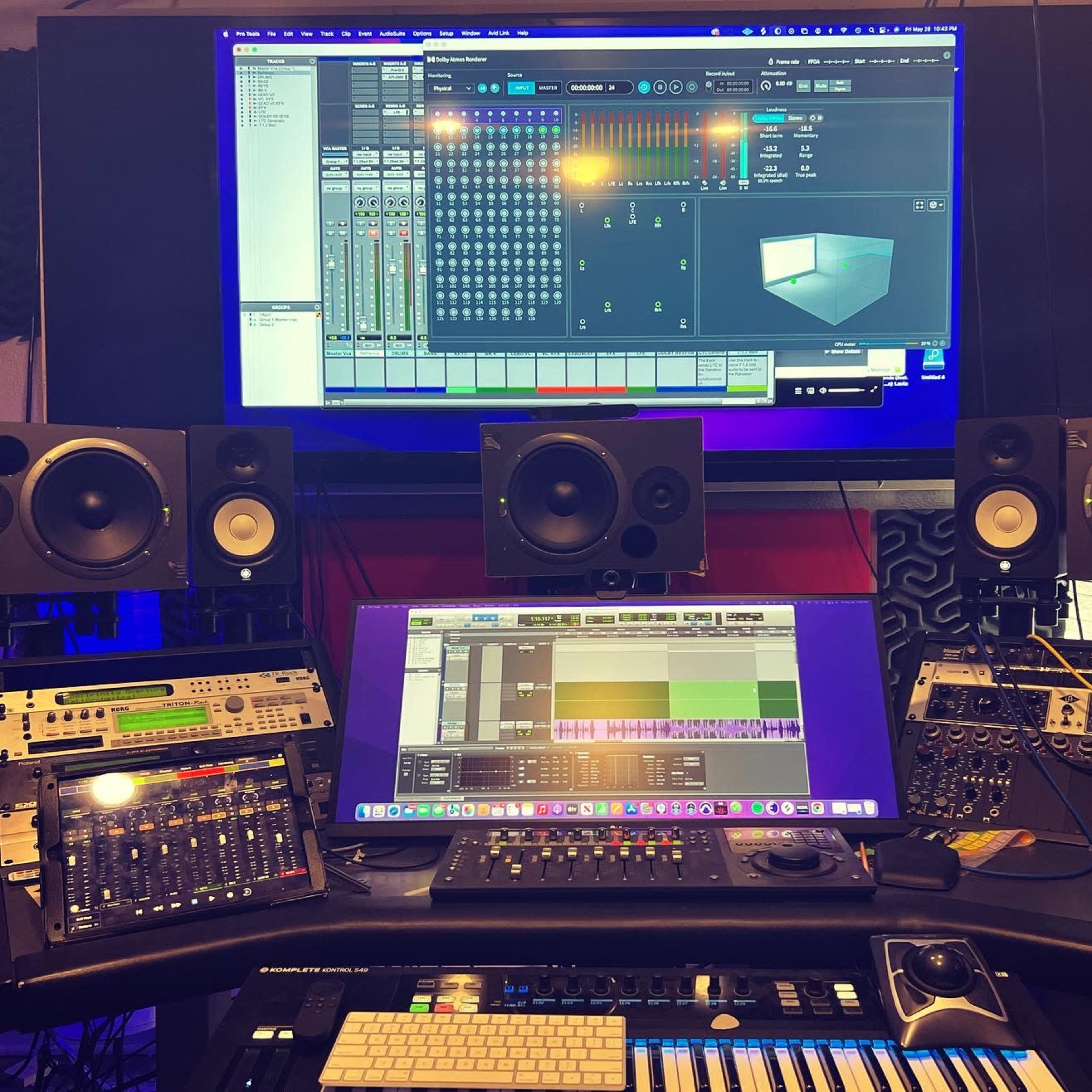 A music production studio with multiple audio speakers, a control surface, a keyboard, and a computer monitor displaying audio mixing software.