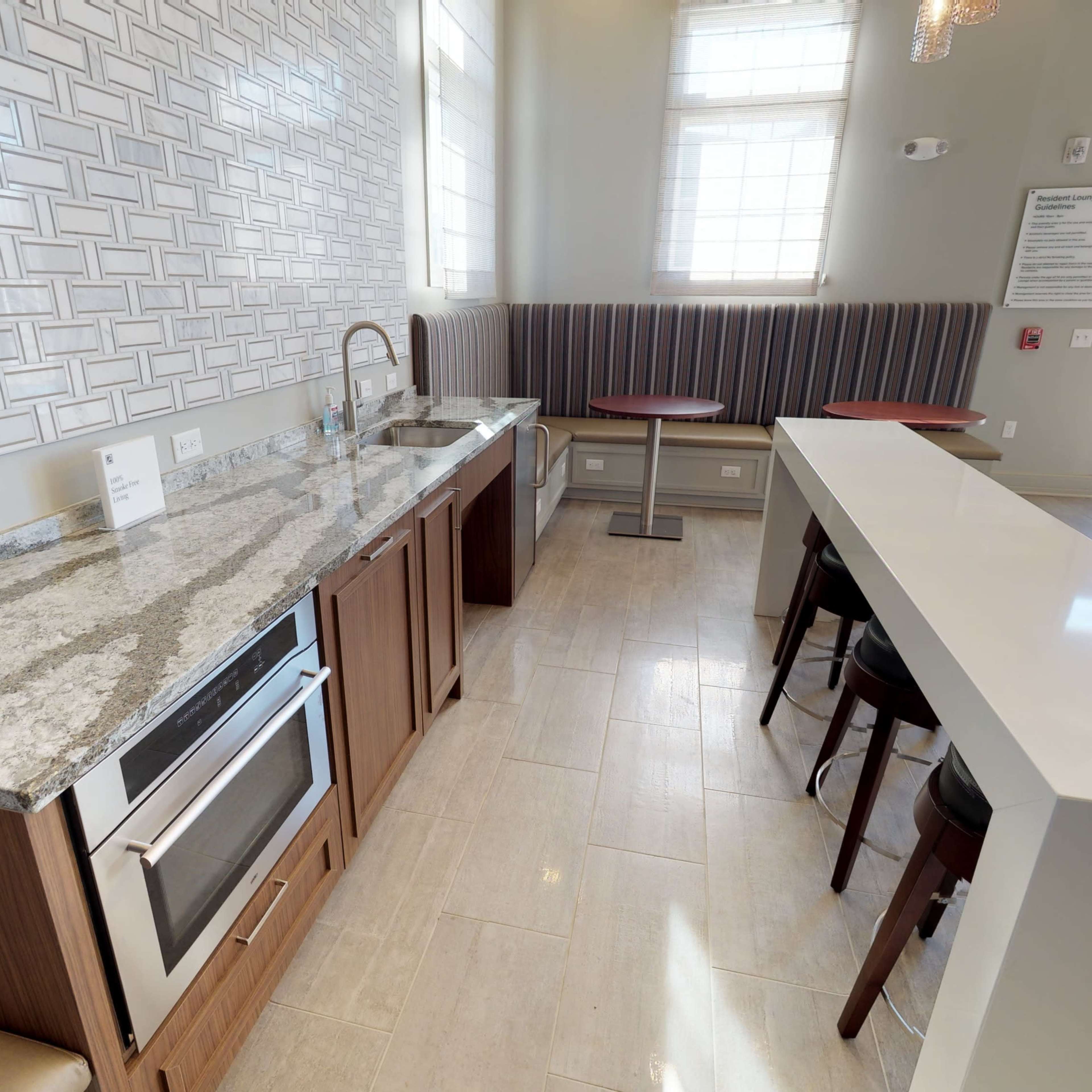 A modern kitchen area with a granite countertop, stainless steel appliances, and high-top seating near large windows.