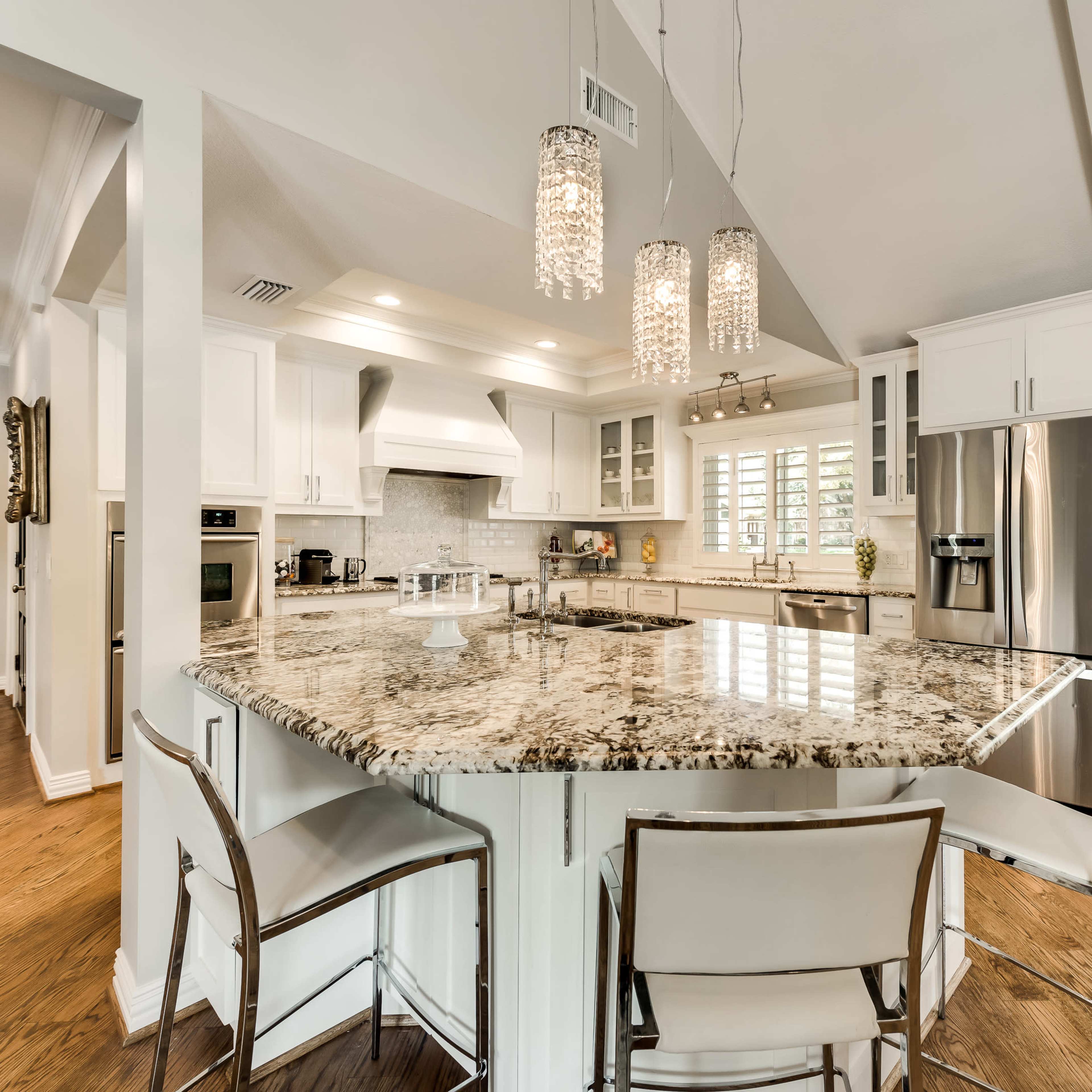 A modern kitchen with a large granite island, white cabinetry, and pendant lighting.