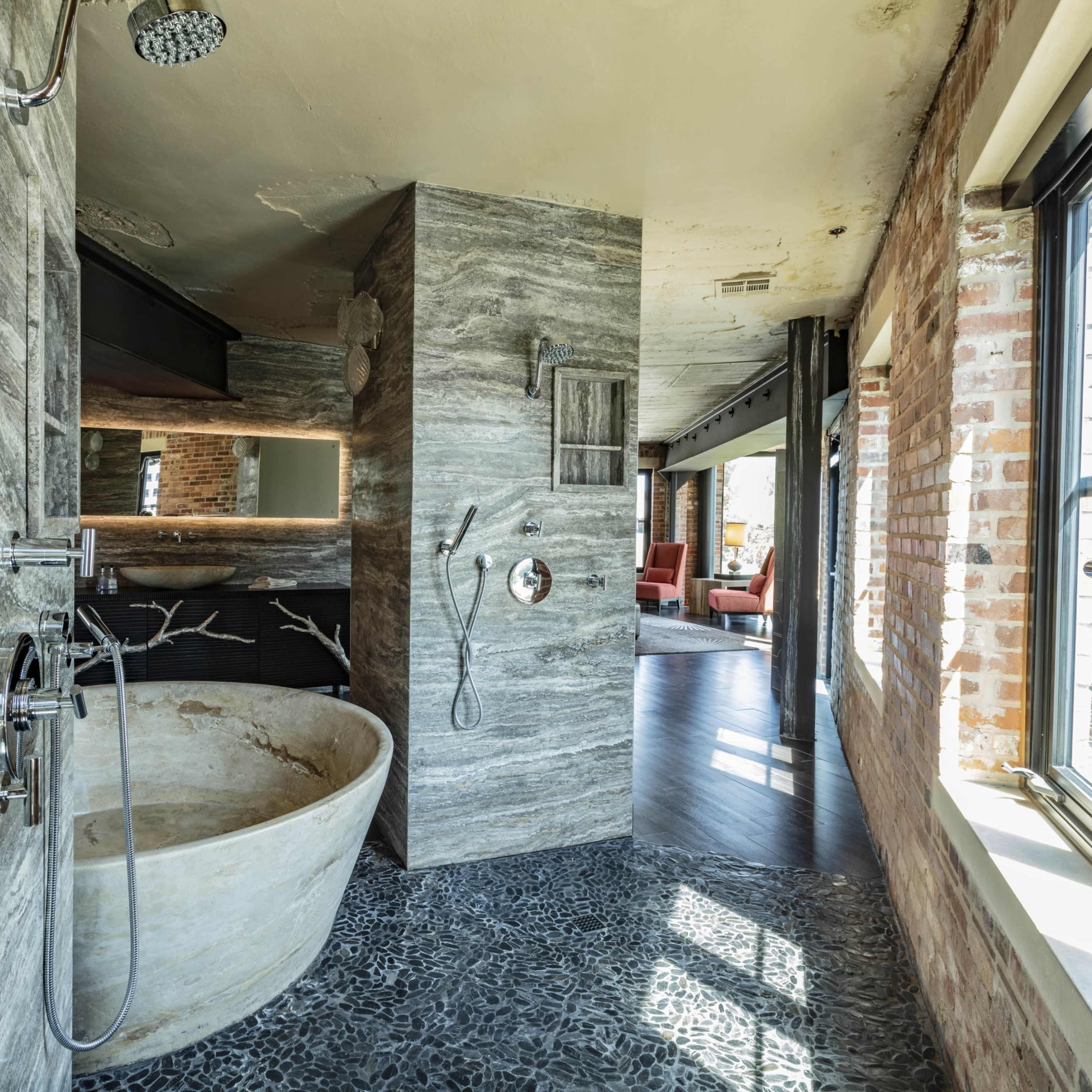 A modern bathroom featuring a large stone bathtub, textured stone walls, and wide windows allowing natural light.