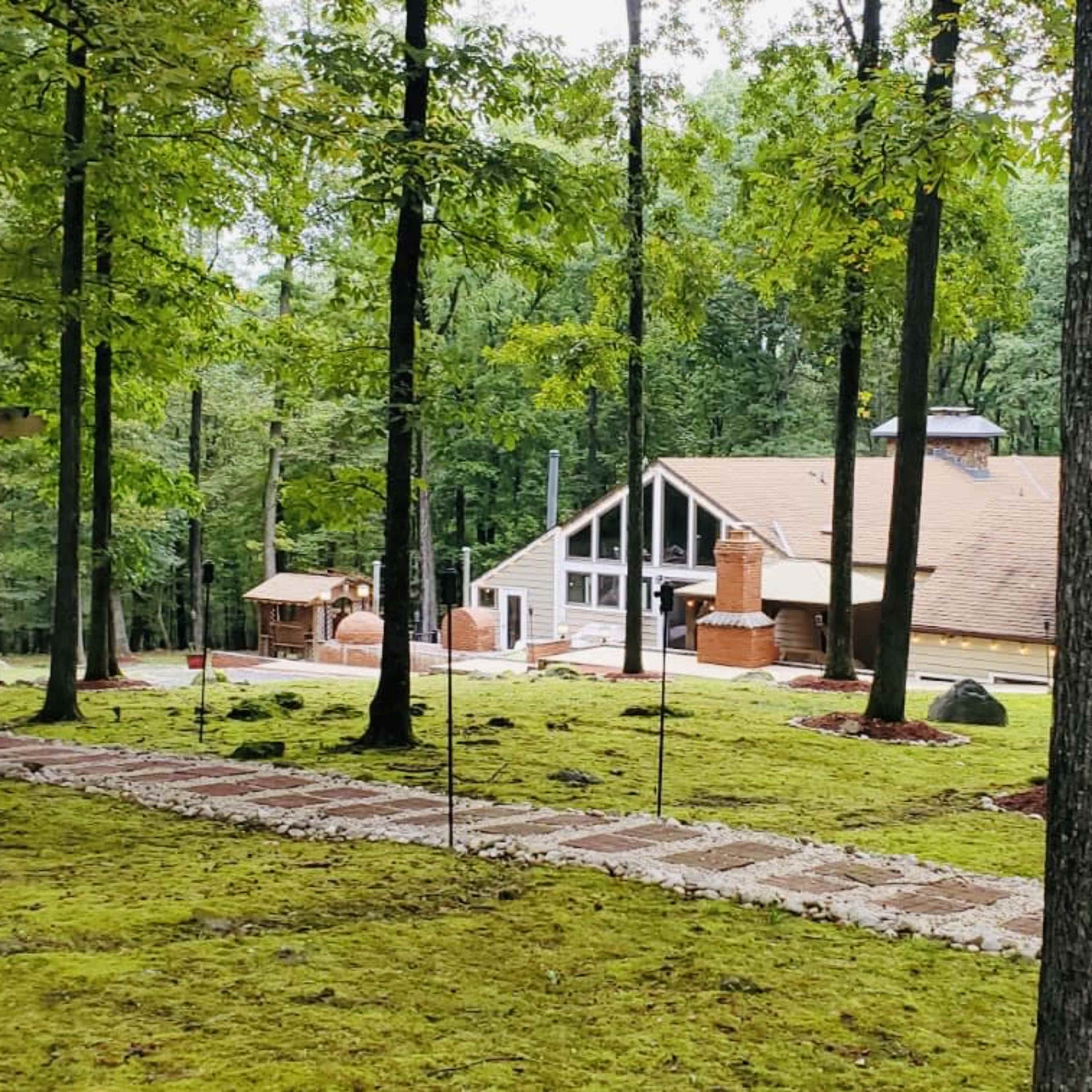 A spacious house is surrounded by trees, with a stone pathway leading to it through a grassy area.