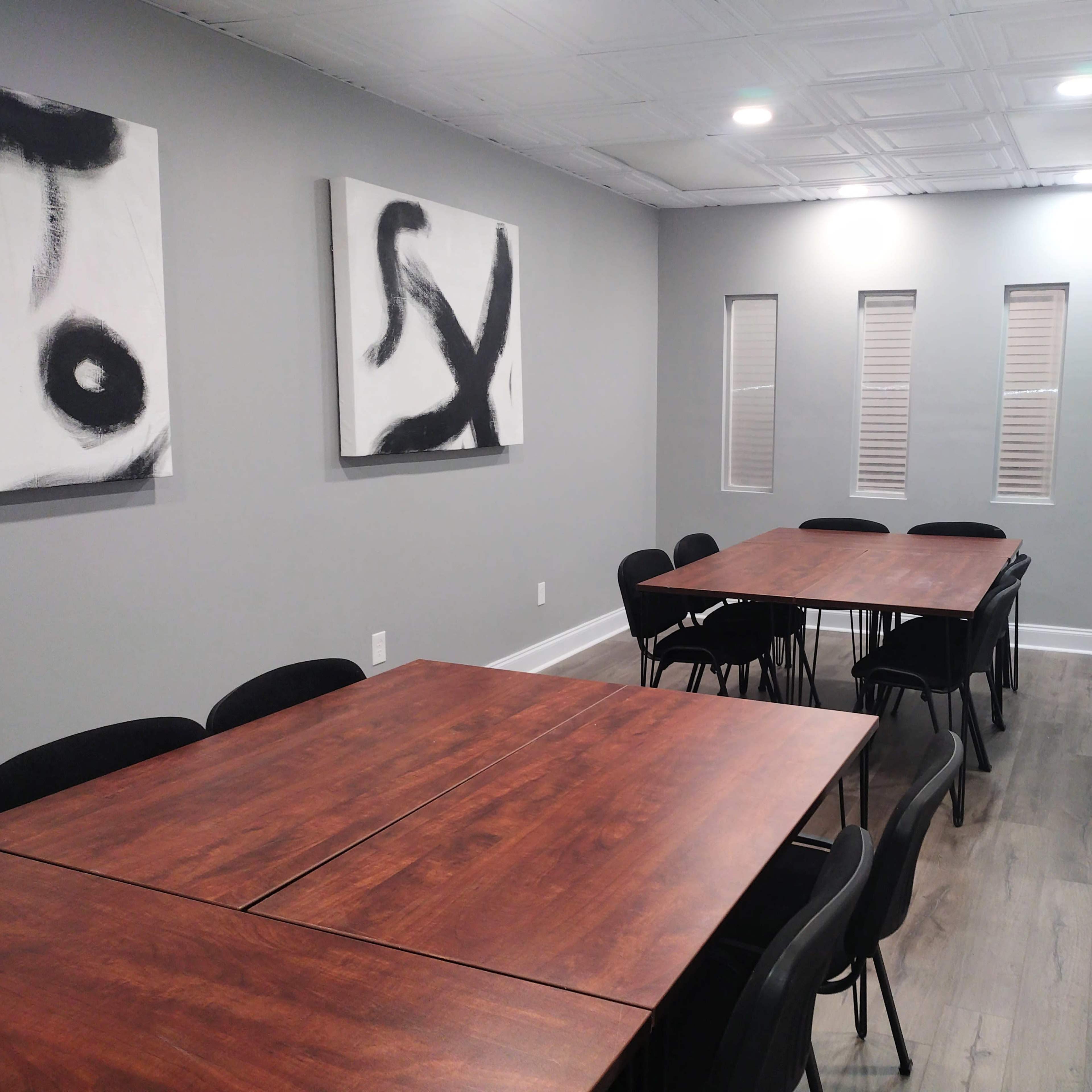 A meeting room with four wooden tables arranged in rows and black chairs, featuring abstract black-and-white artwork on the walls.