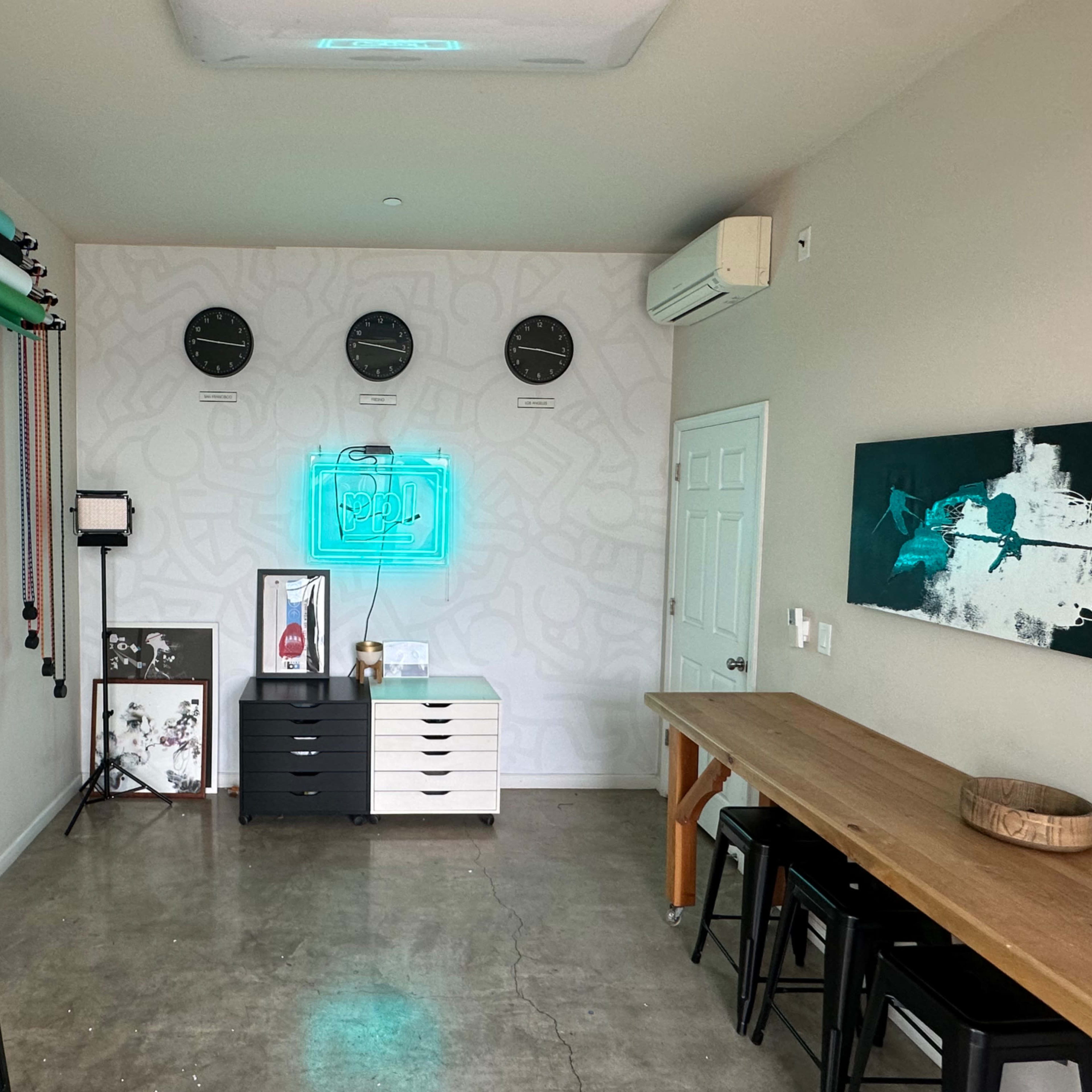 A modern studio or workspace featuring a large table, art on the walls, multiple clocks, and a color backdrop setup.