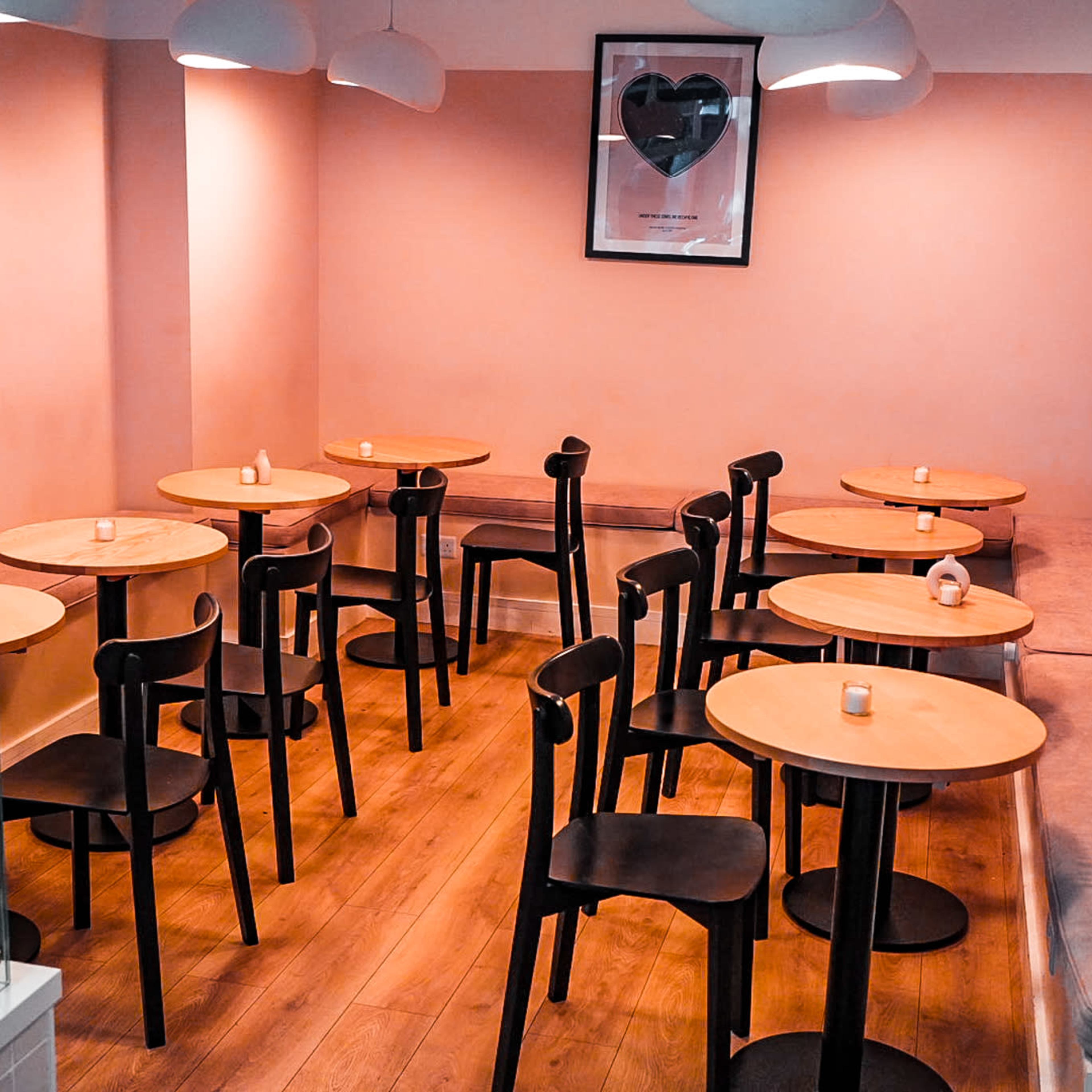A cozy cafe interior with several small round tables and chairs arranged in a simple layout, illuminated by soft overhead lighting.