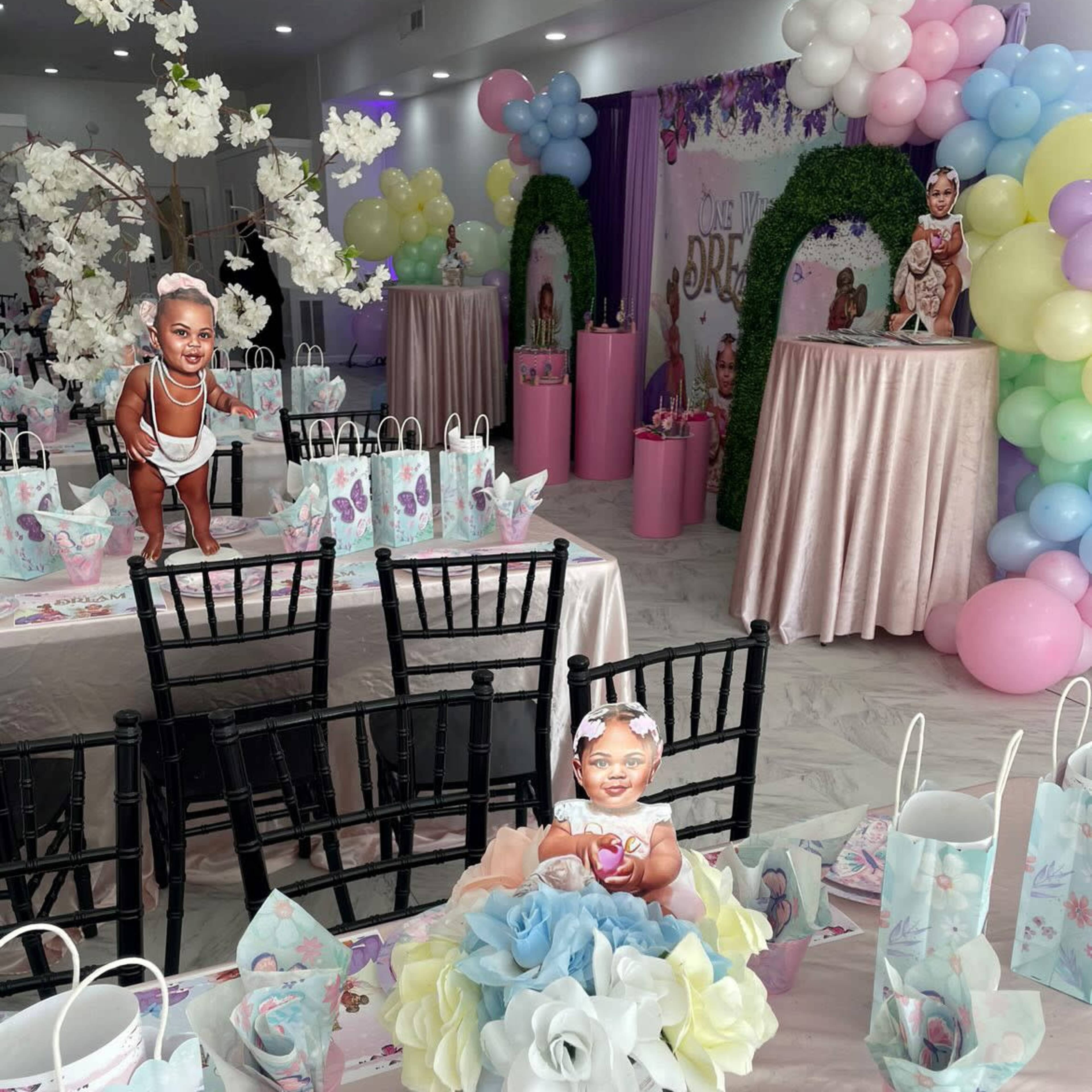 The scene depicts a decorated party venue with tables set for a celebration, featuring pastel colored balloons, floral arrangements, and themed tableware.
