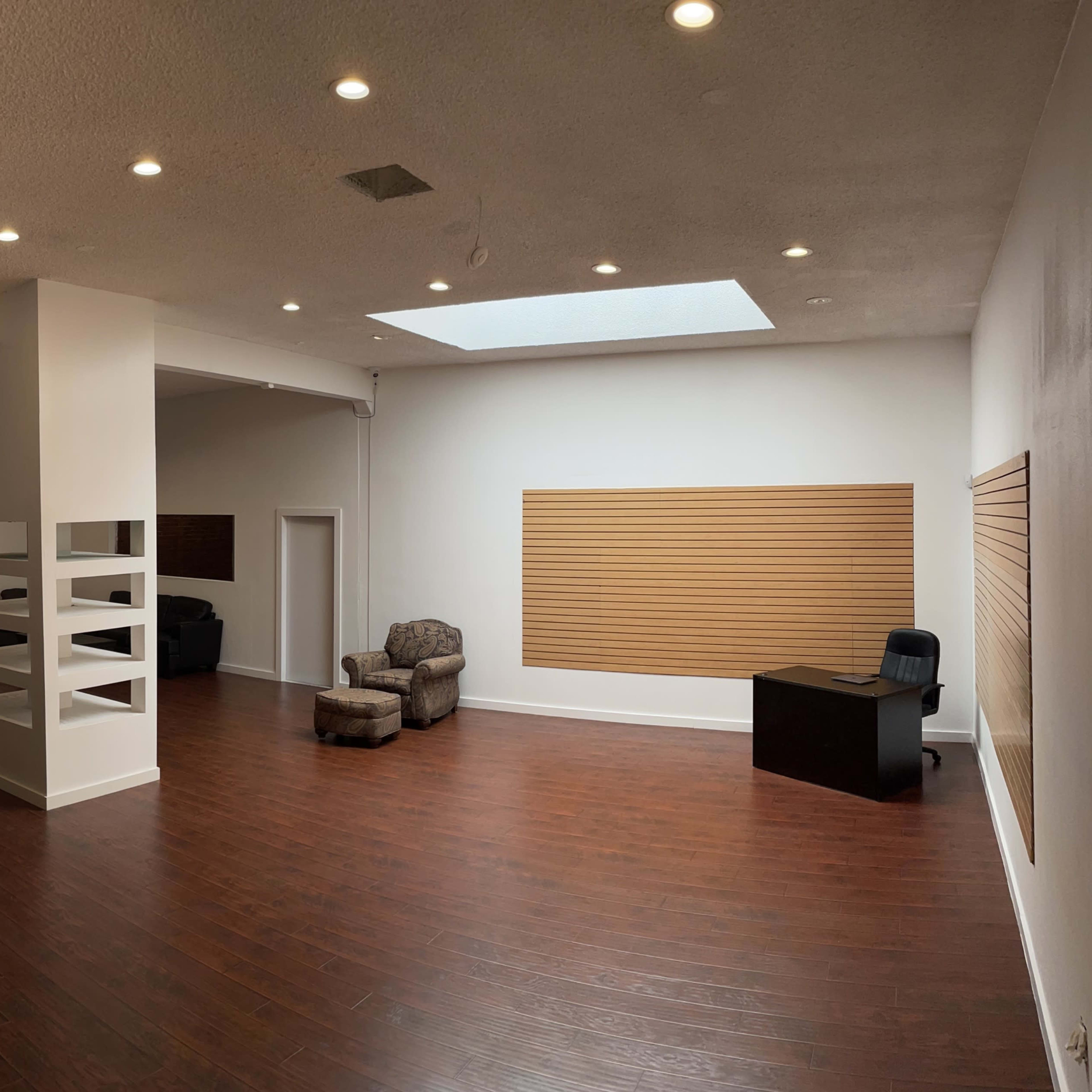 An empty and spacious room with hardwood floors, two seating areas, and a large skylight.