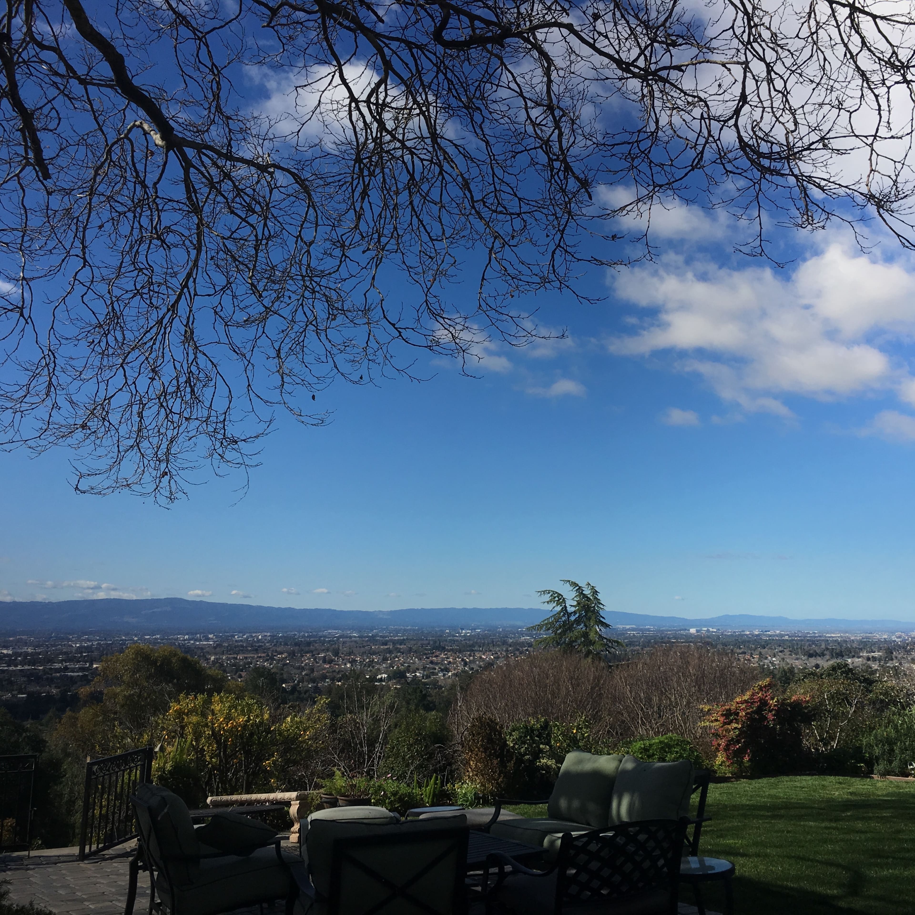 A view of a valley and distant mountains under a partly cloudy sky, framed by tree branches in the foreground.