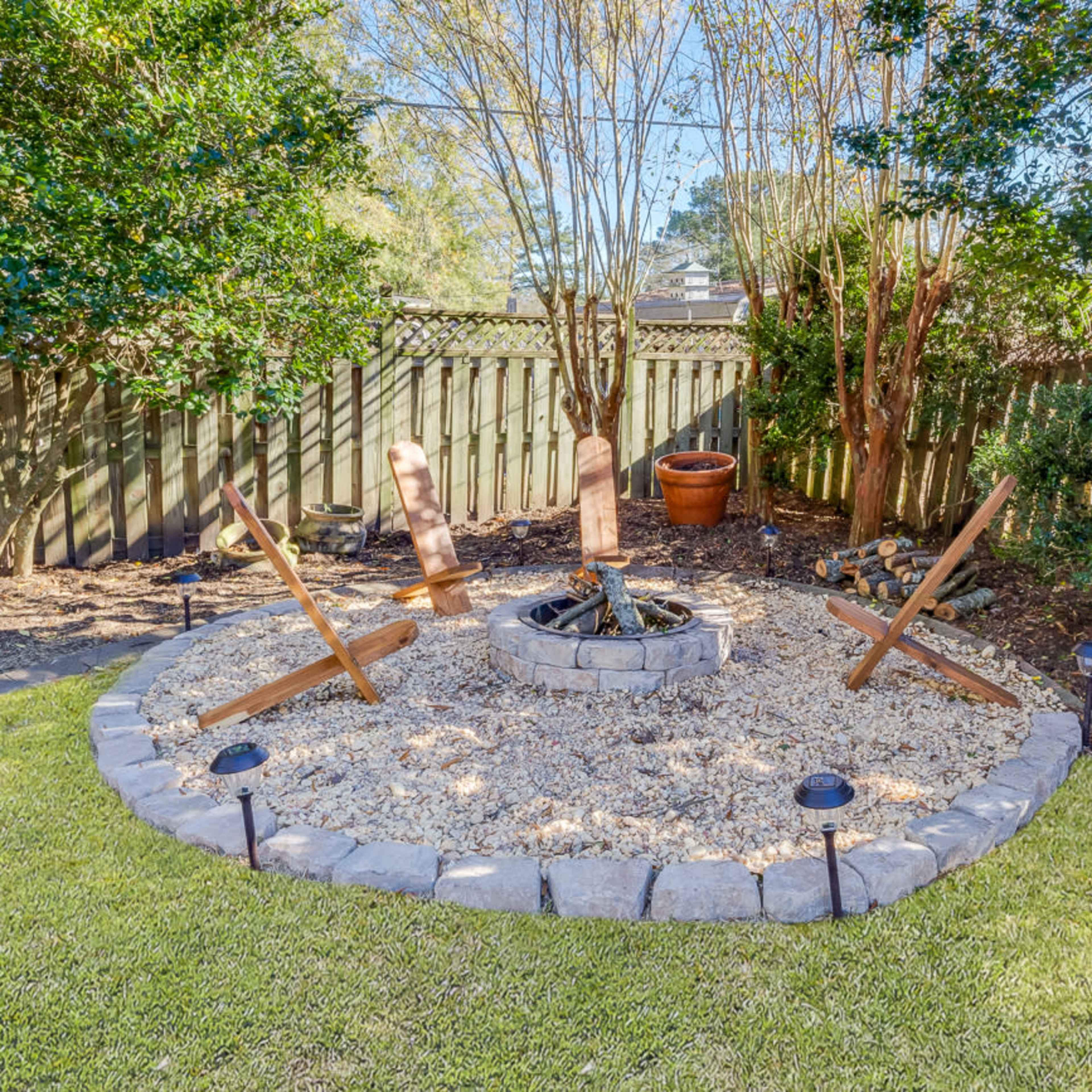 A circular fire pit surrounded by a stone border, with wooden logs arranged for seating in a landscaped backyard.