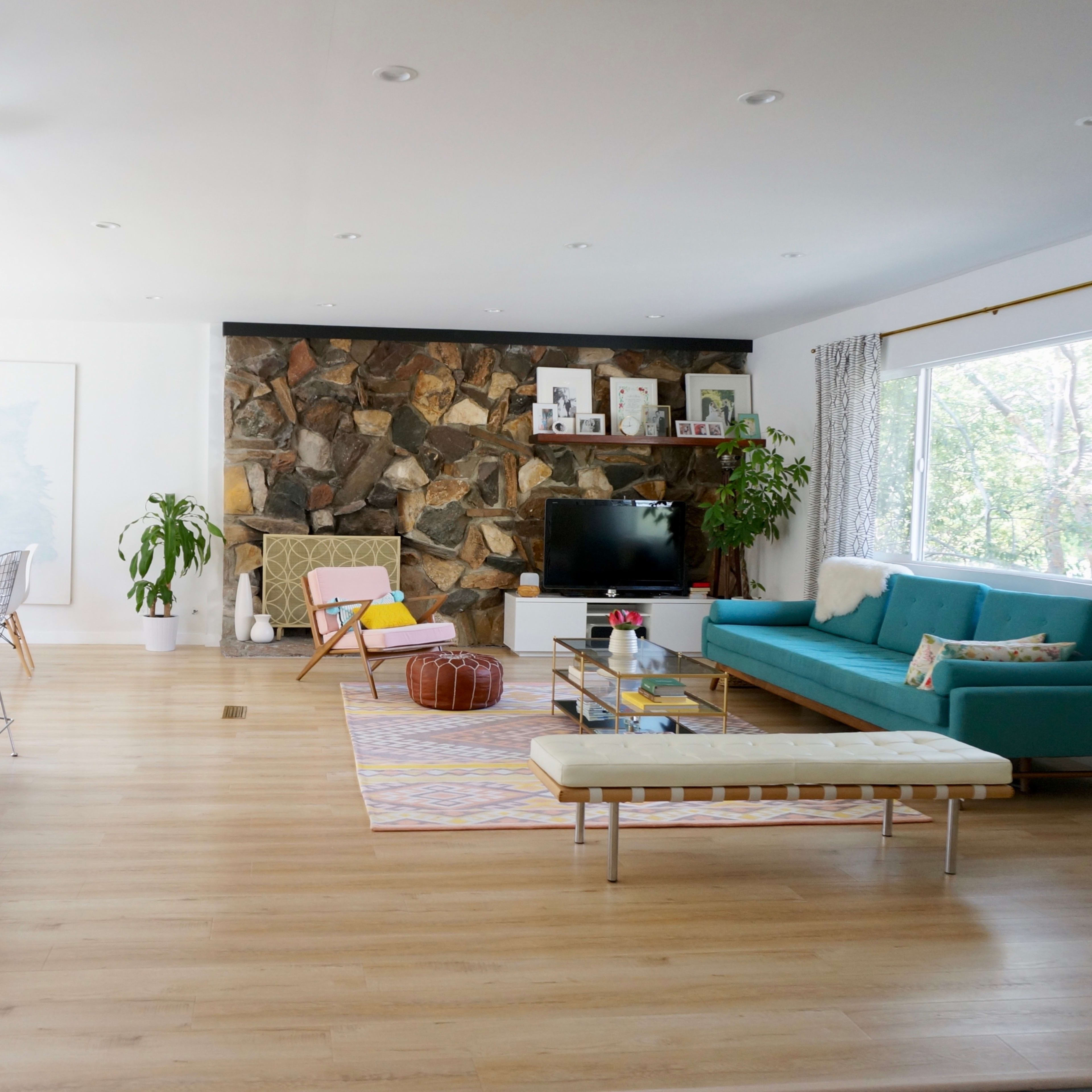 A modern living room with a stone wall, a teal sofa, a flat-screen TV, and a kitchen bar with stools.