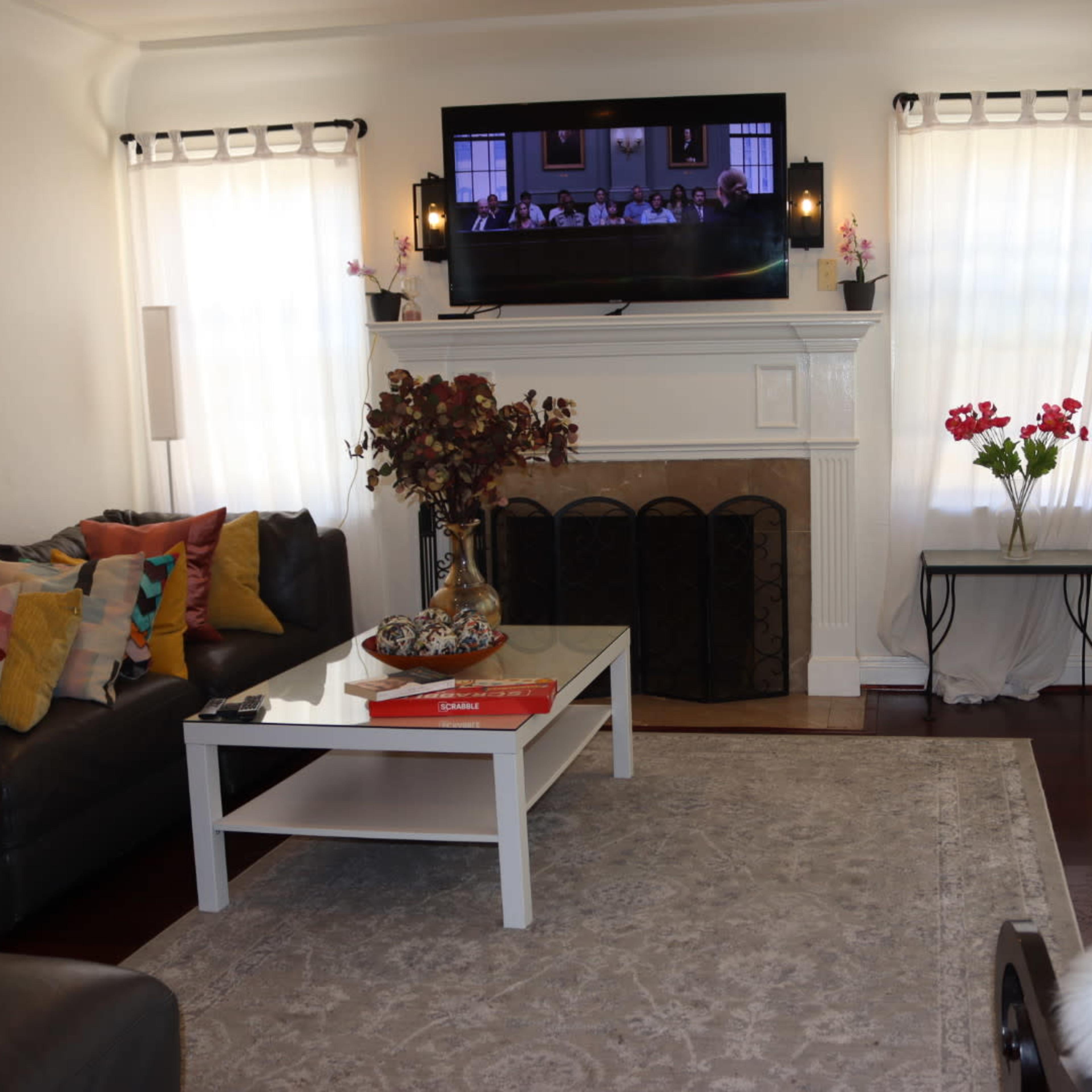 A living room with a black leather sofa, a white coffee table, and a television mounted above a fireplace.