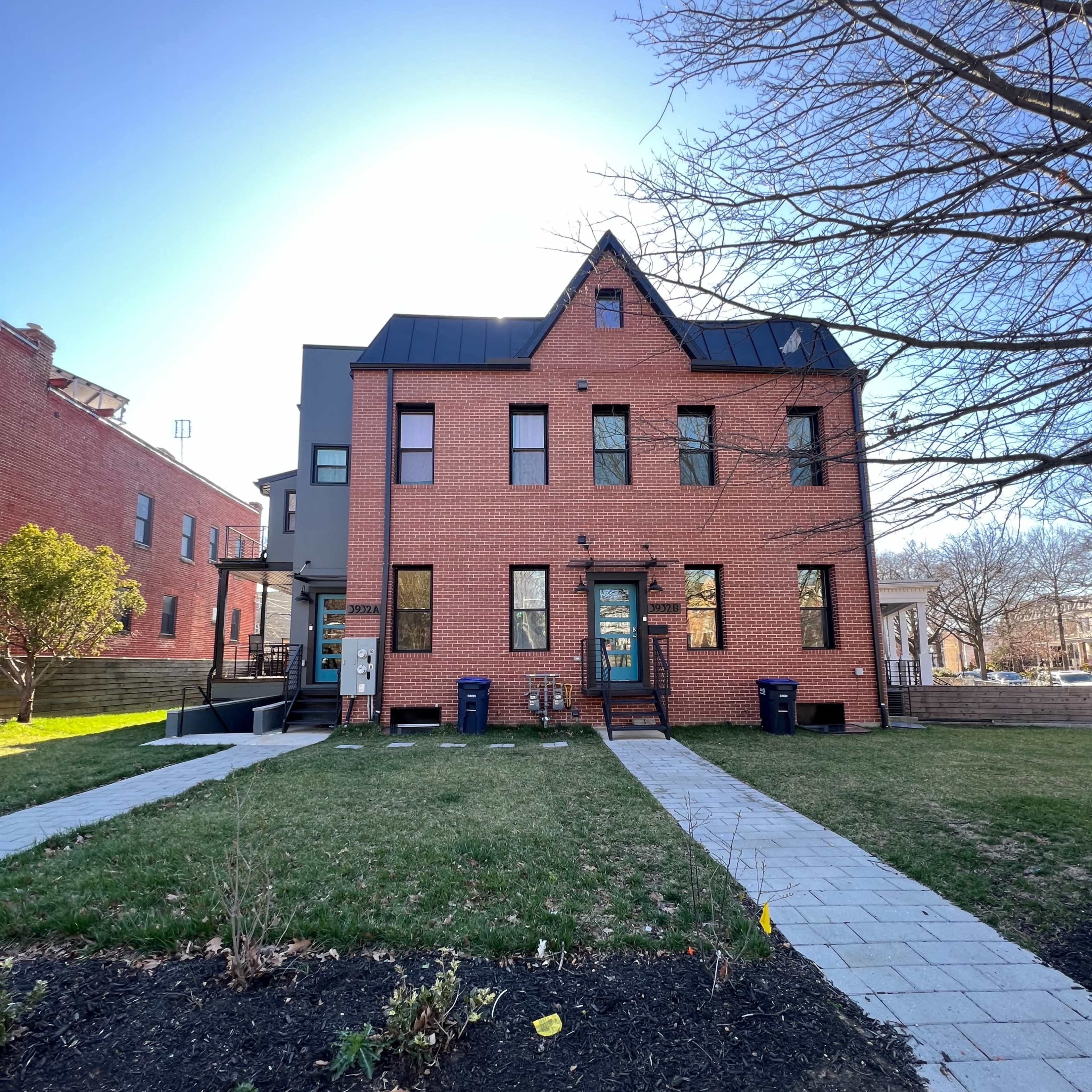 A two-story brick house with a black metal roof and a front yard featuring a walkway and some landscaping.