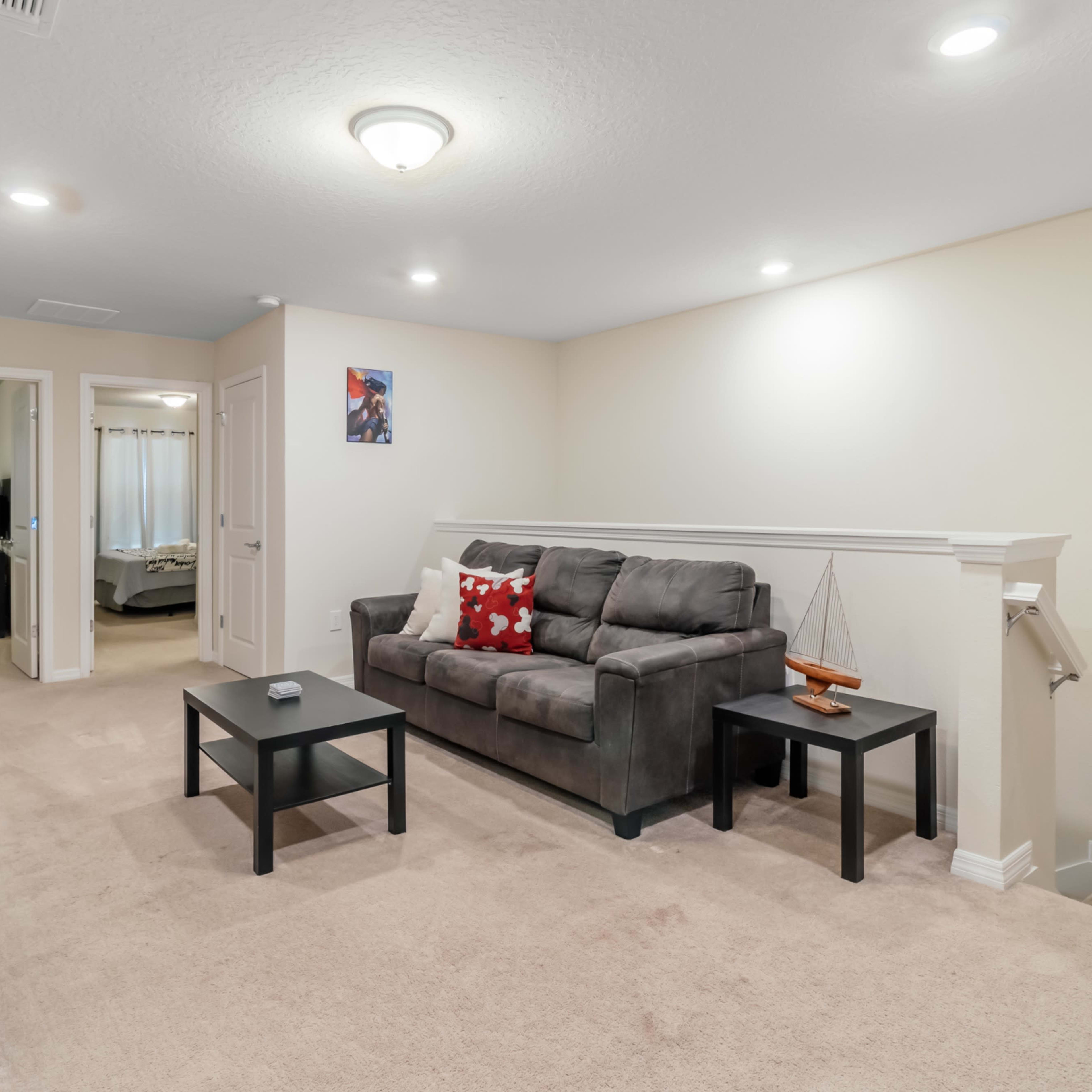 A cozy living area with a gray sofa and two black tables, set on beige carpet, leading to a doorway that connects to another room.