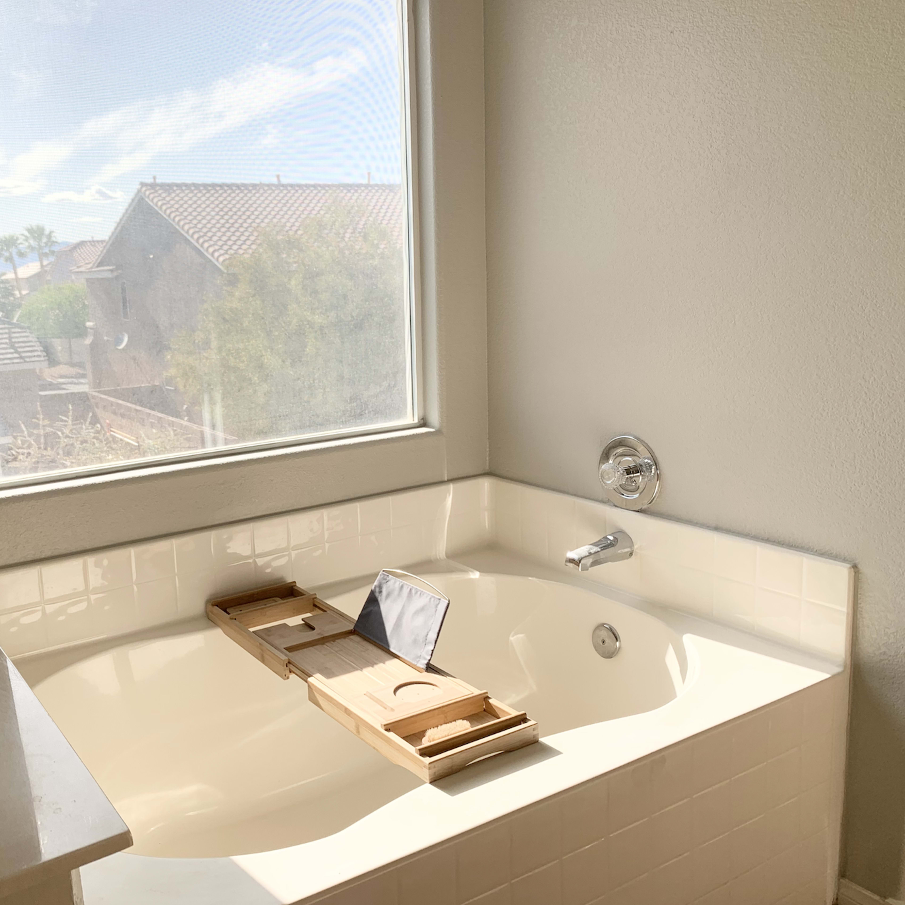 A bathtub next to a large window with a view of rooftops and trees outside.