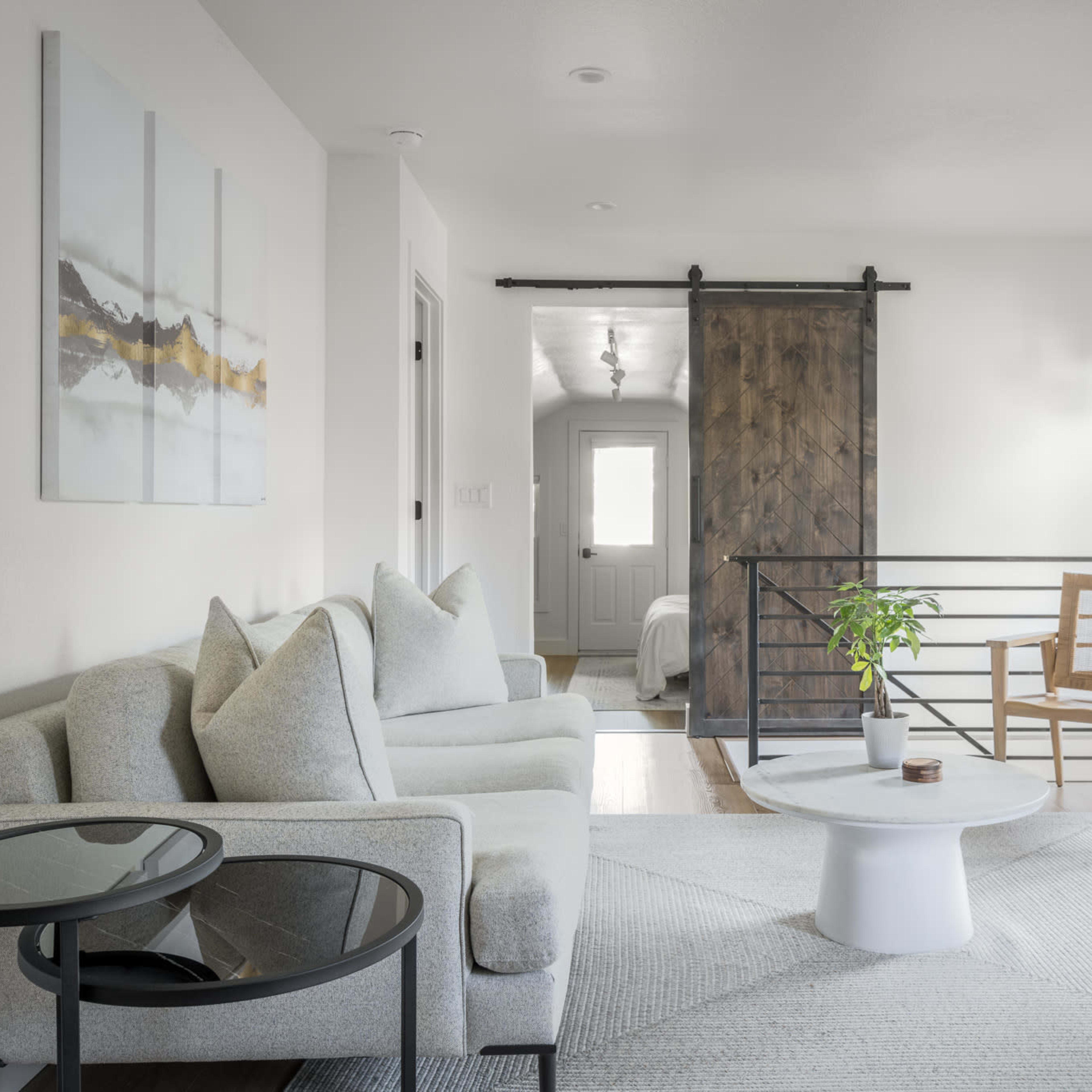 A modern living room with a light-colored sofa, a small round table, and a sliding barn door leading to a bedroom.