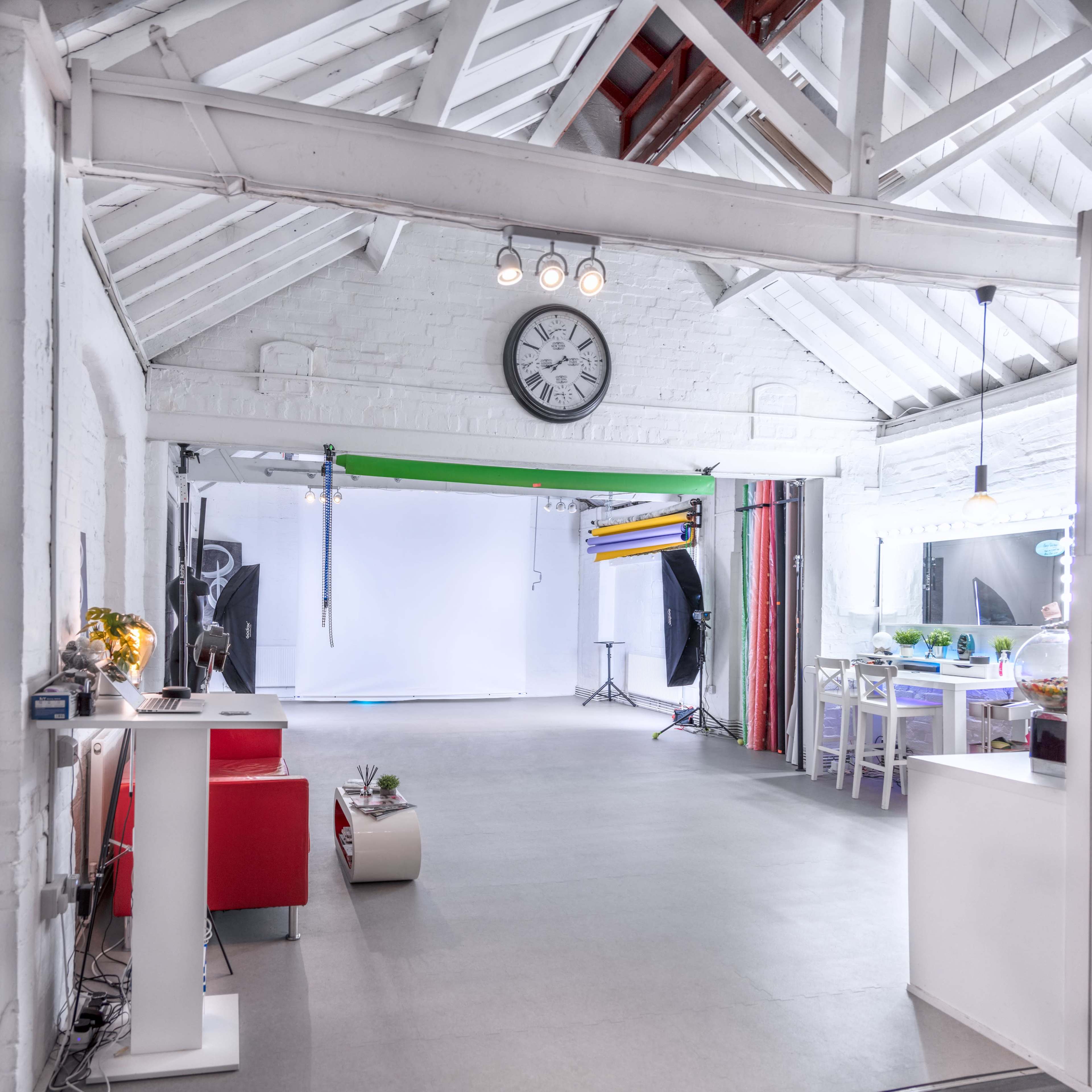 A well-lit photography studio with a large open area and various equipment, including a clock on the wall and a desk with a computer.