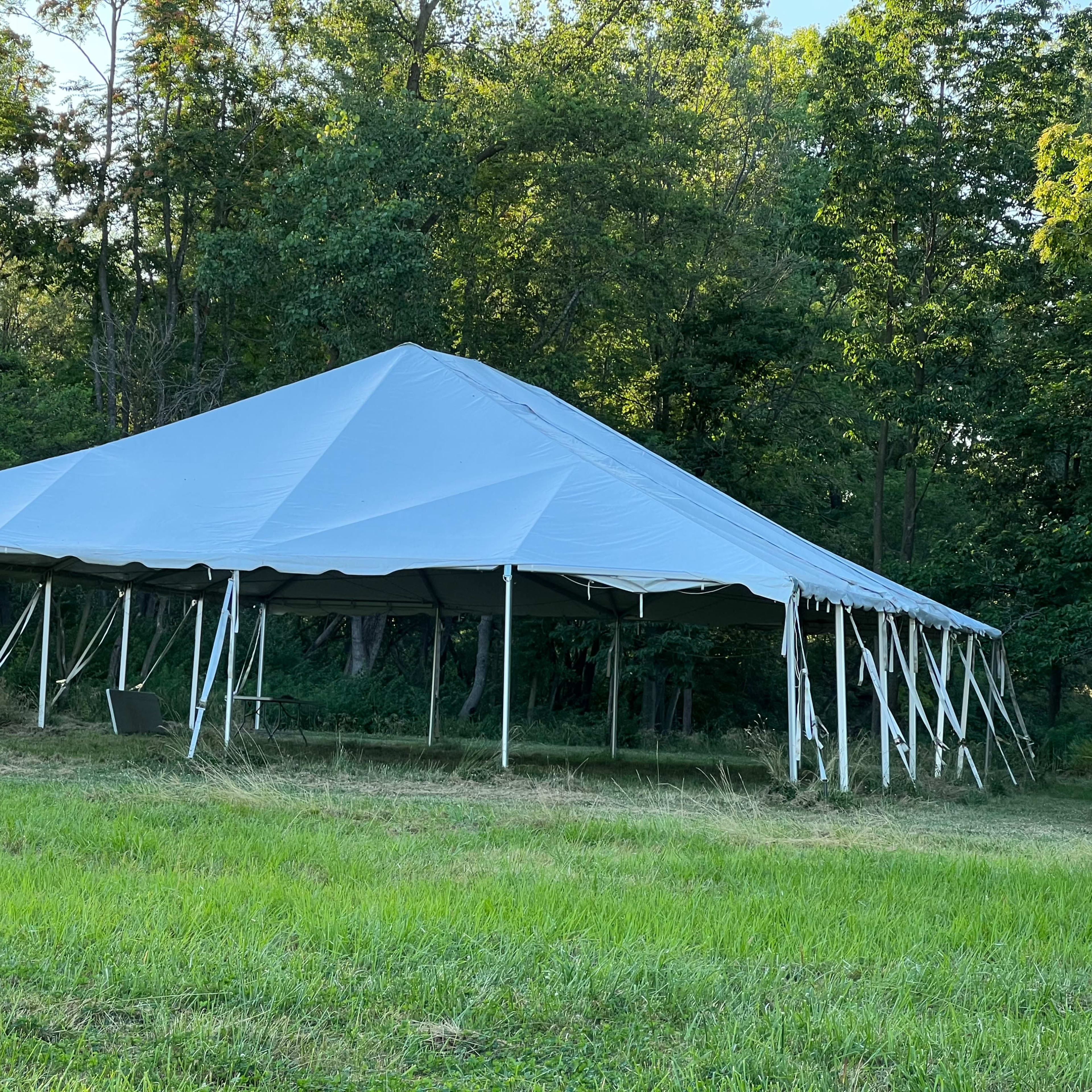 A large white tent is set up on a grassy area surrounded by trees.