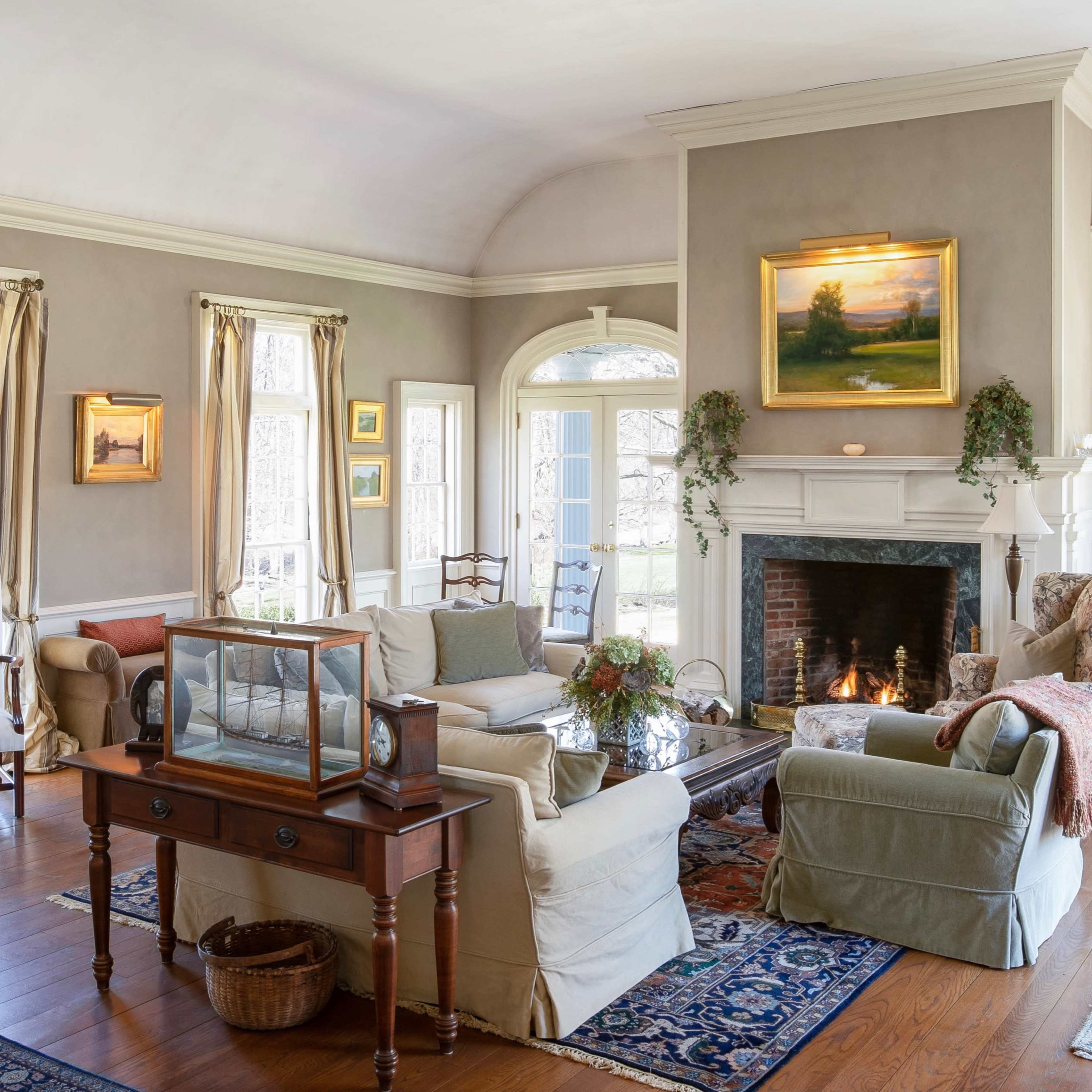 A light-filled living room features a fireplace, comfortable seating, and large windows overlooking a grassy yard.