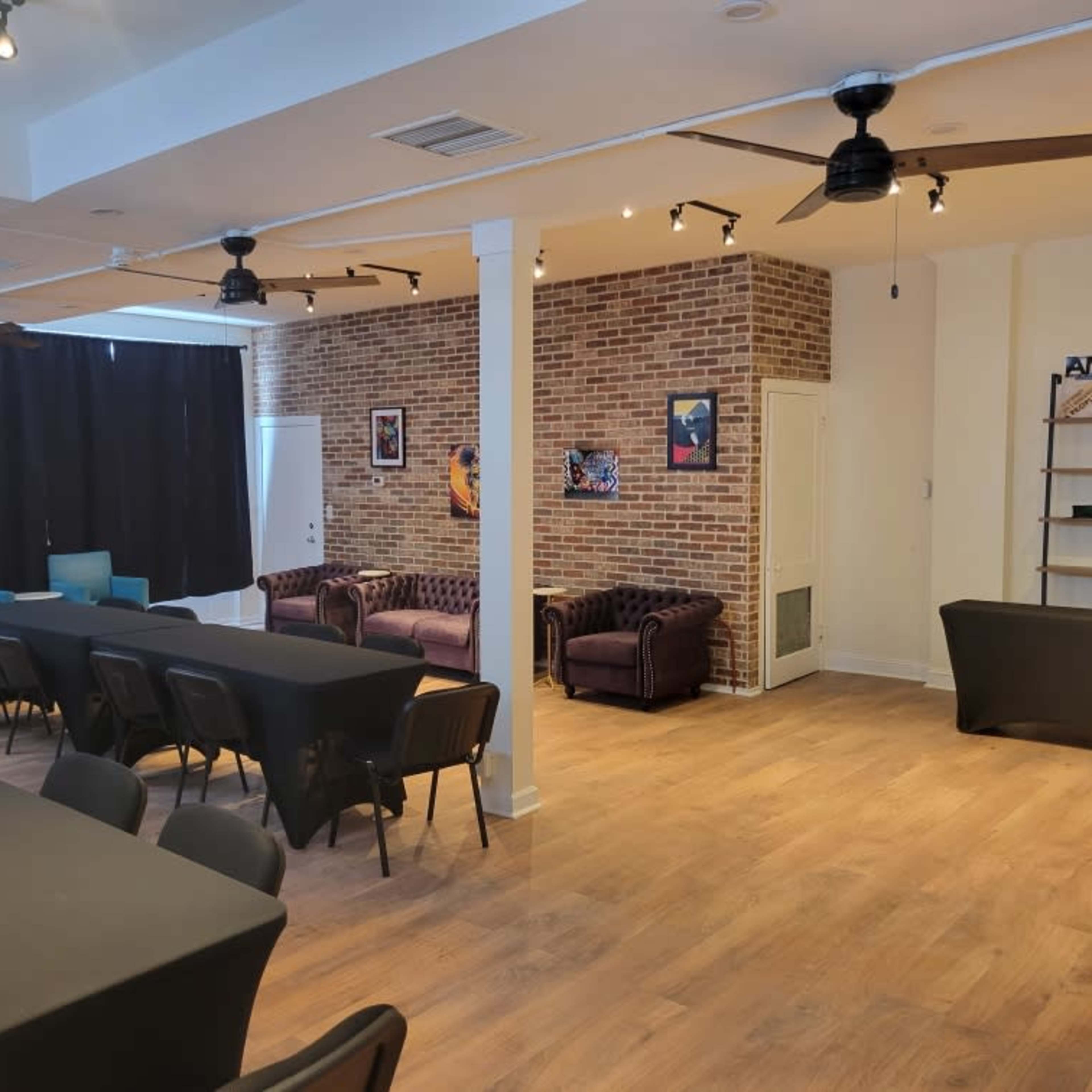 A spacious room with a seating area featuring two sofas, tables arranged with black covers, and a brick wall adorned with framed artwork.