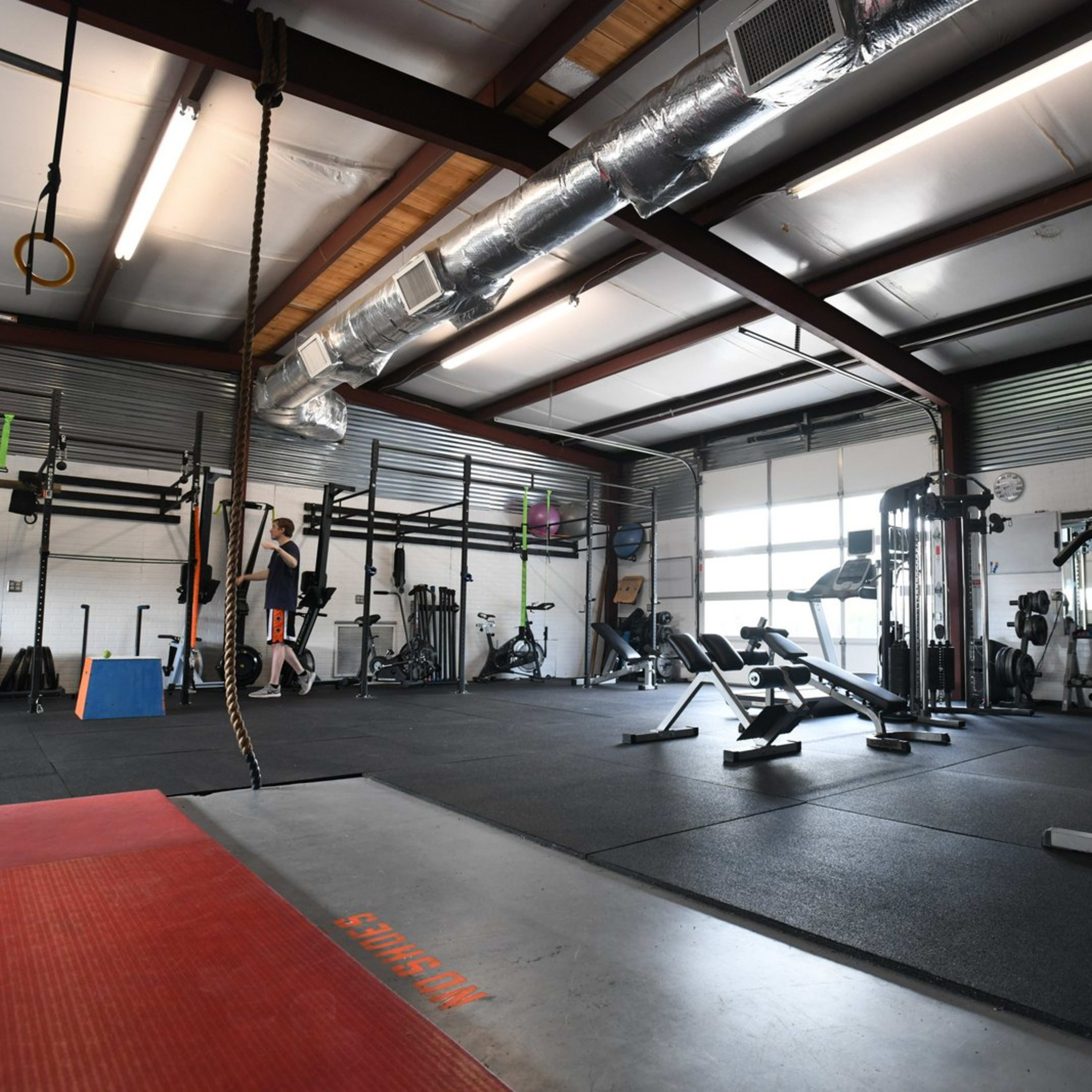 A gym interior with exercise equipment, including weights and benches, and individuals performing workouts in a spacious, well-lit area.