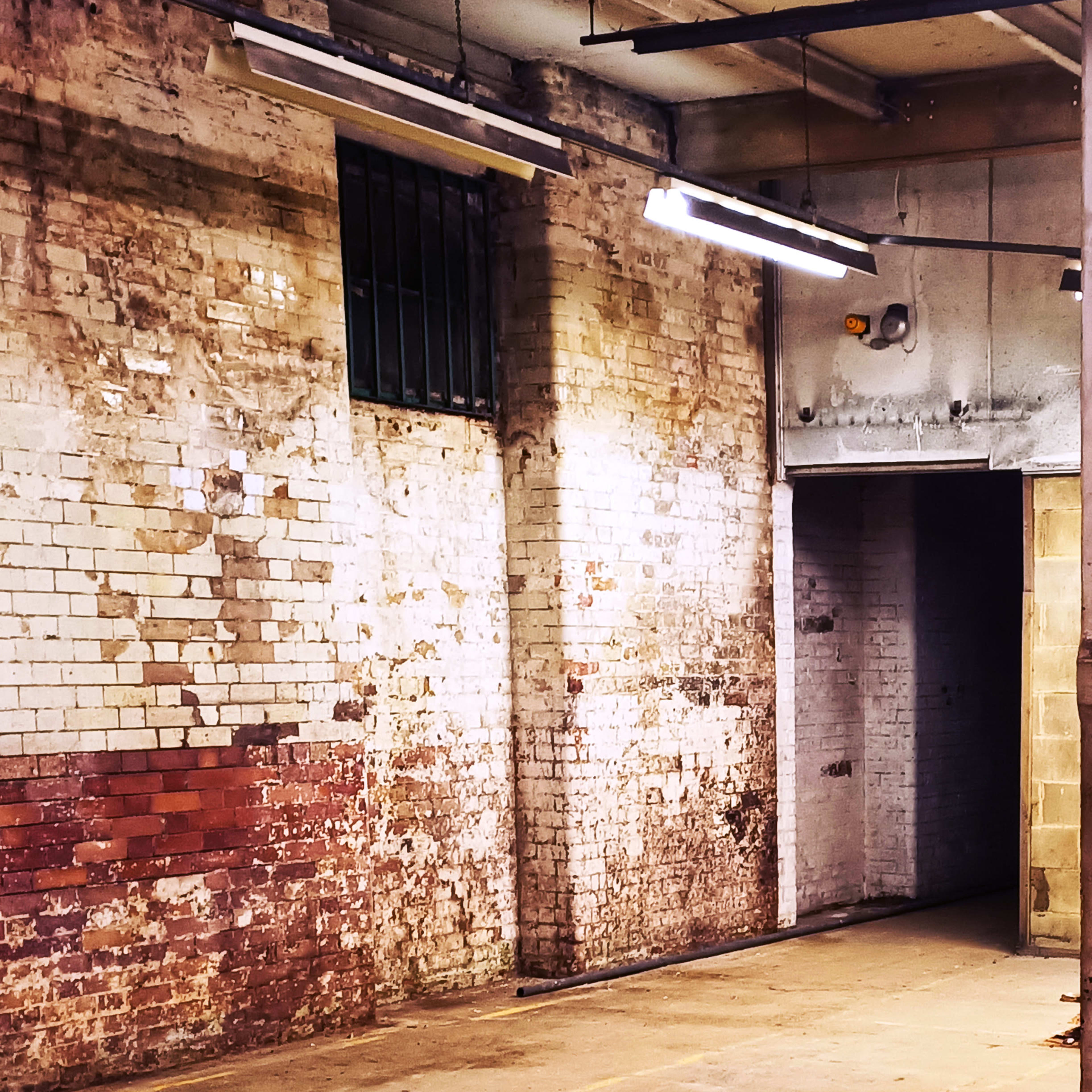 An industrial space with exposed brick walls and a doorway leading into a darker area.